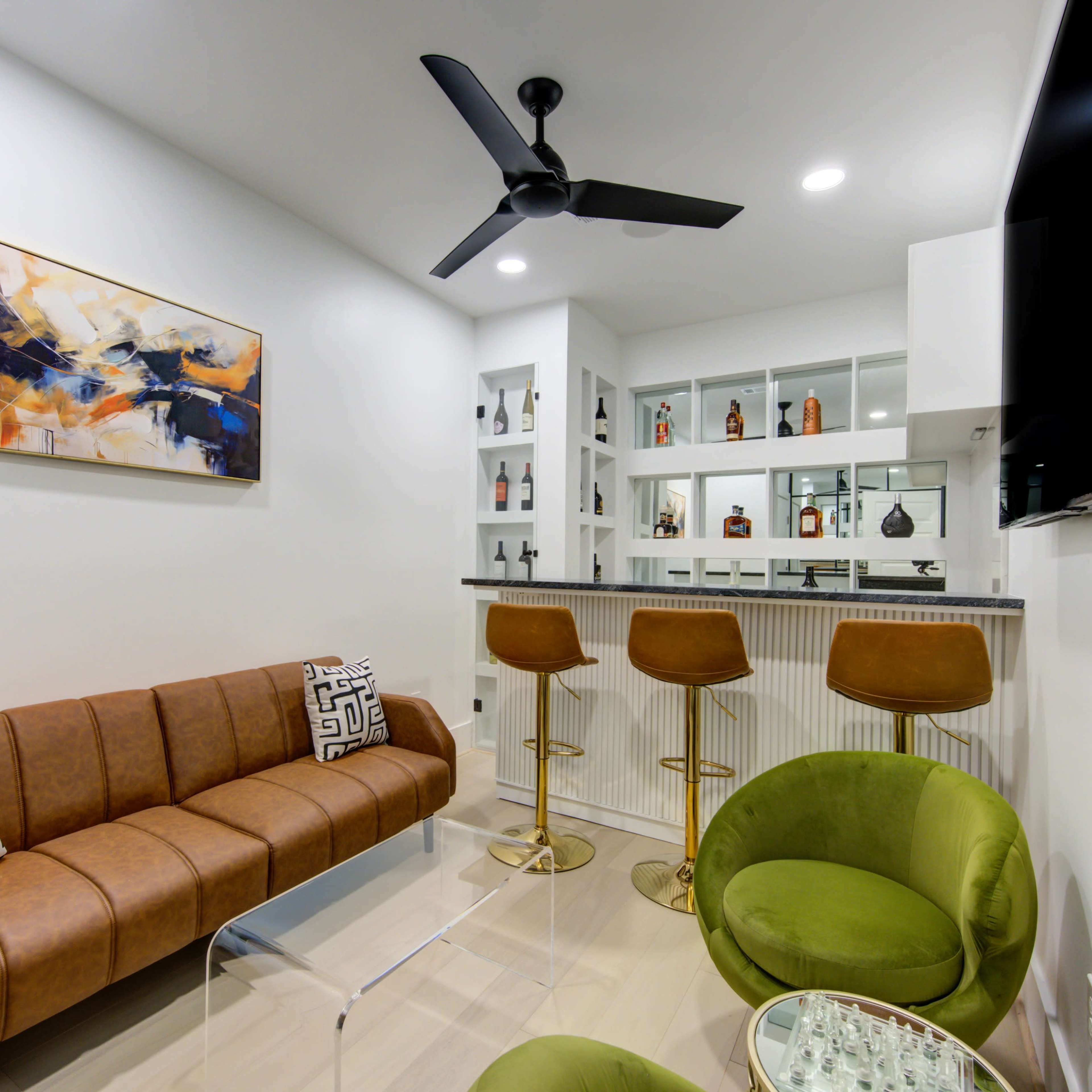 A modern lounge area with a brown sofa, two green chairs, and a well-stocked glass bar in the background.