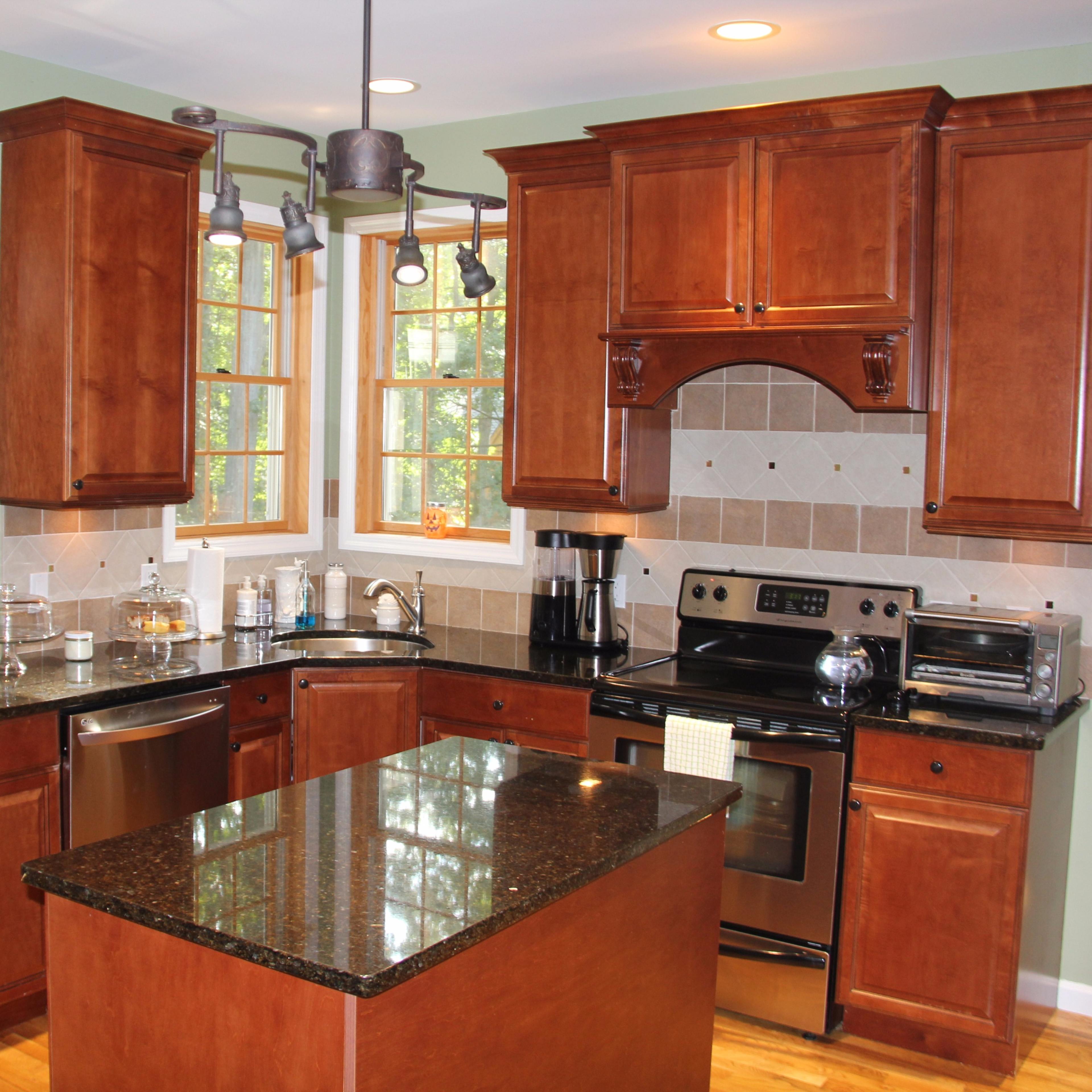 A modern kitchen with wooden cabinets, black granite countertops, and stainless steel appliances, set in a light-filled environment with large windows.
