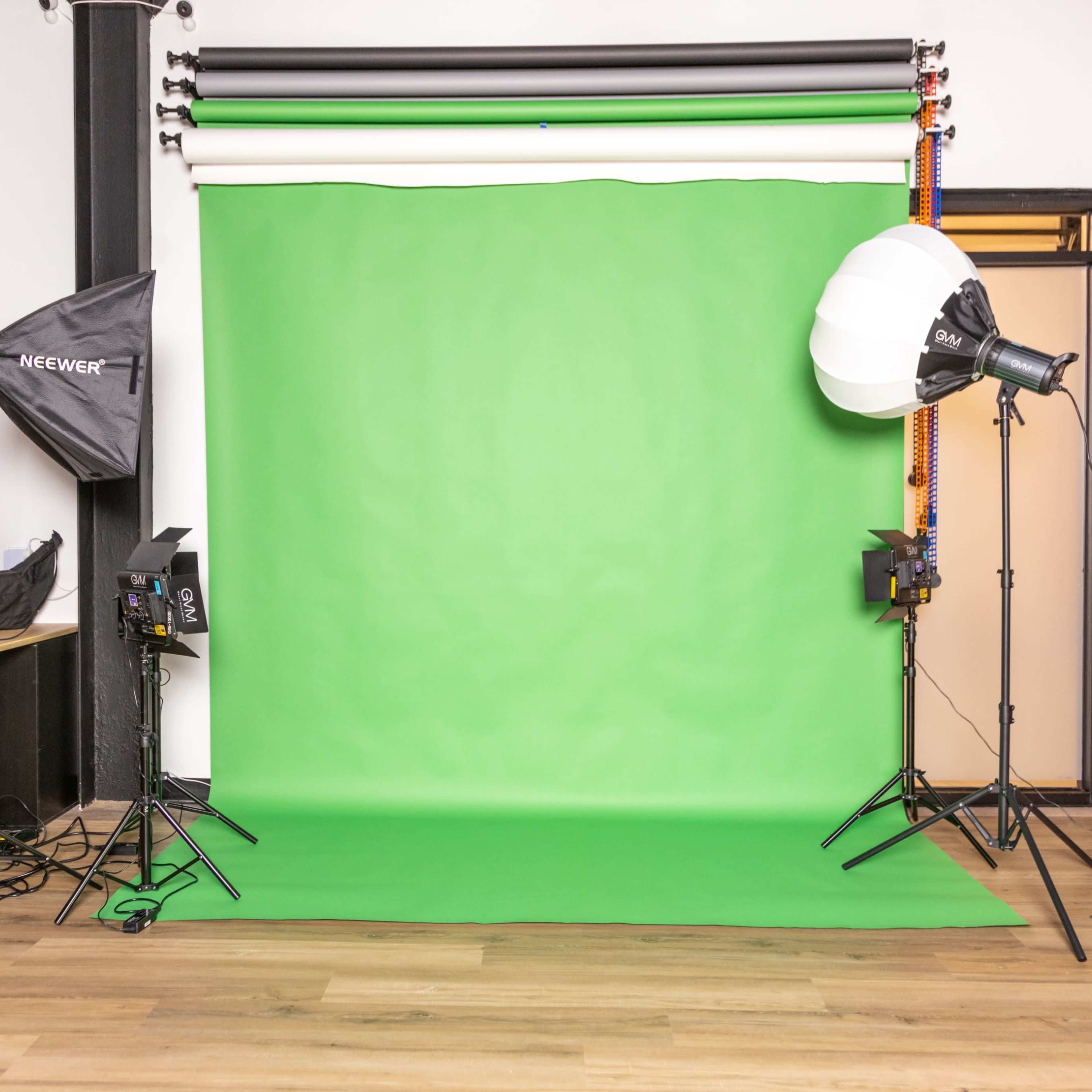 A photo studio setup with a green backdrop, lighting equipment, and an empty work area in the background.