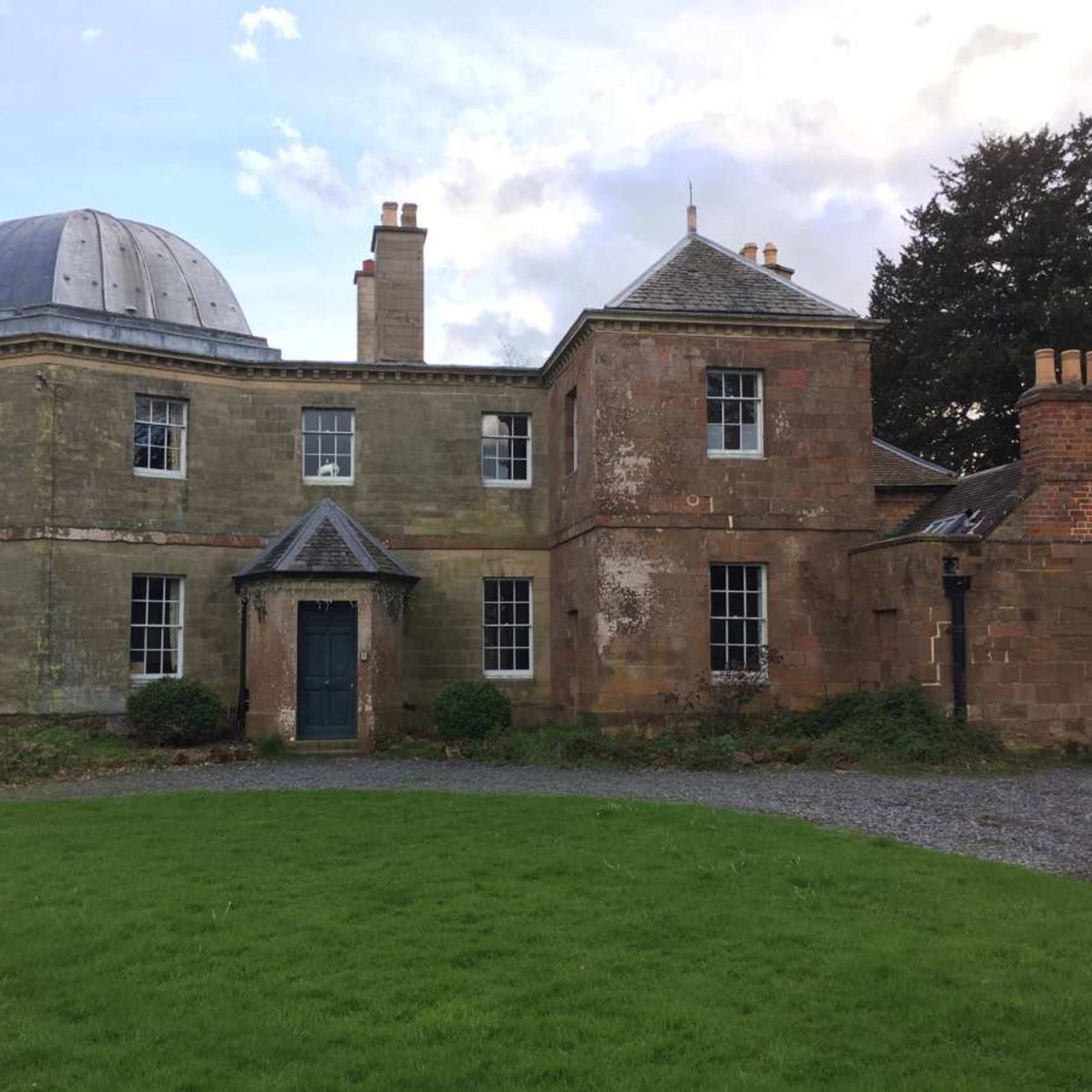 A classical-style house with a dome-shaped roof and multiple chimneys, surrounded by a grassy area.
