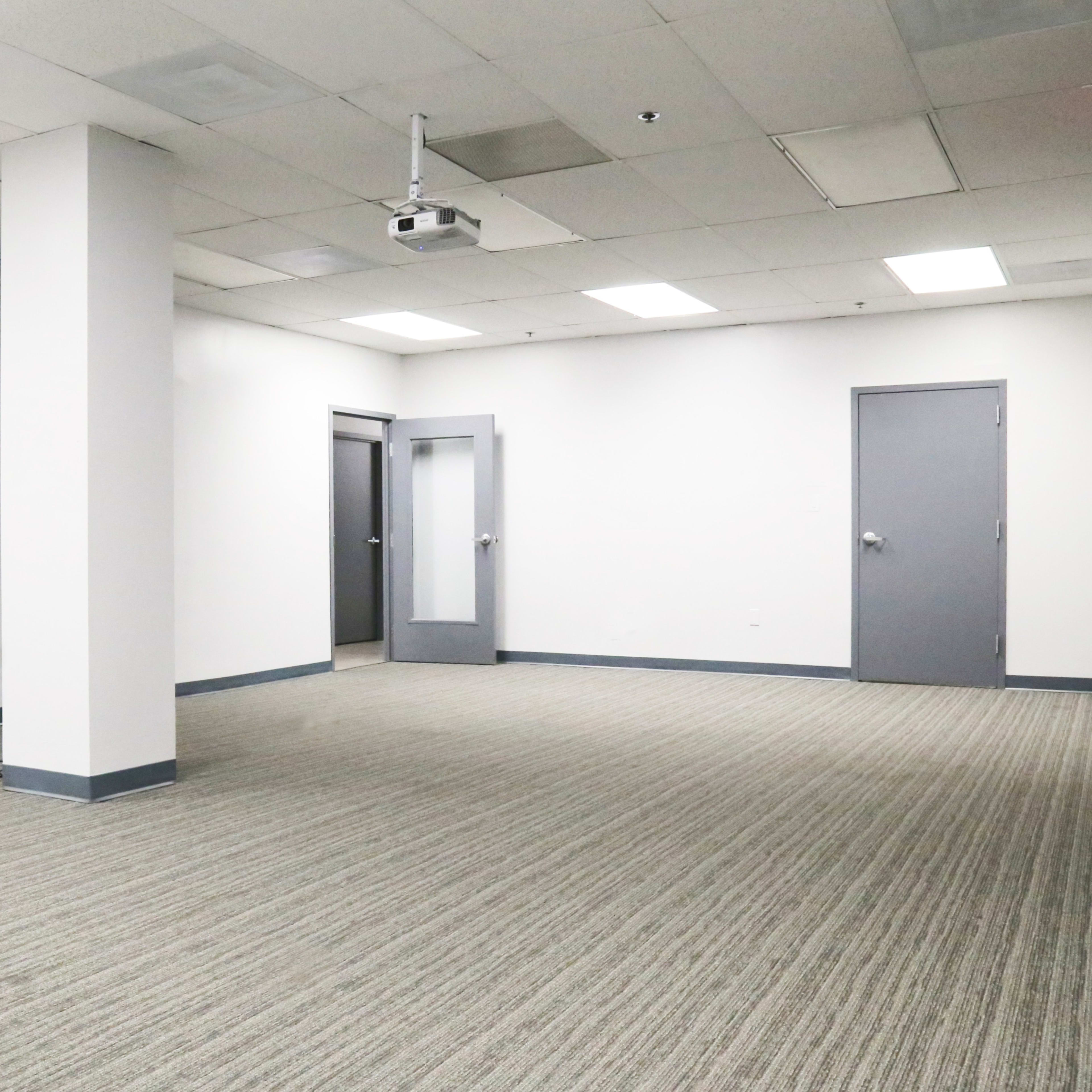 An empty room with gray carpet, white walls, and a door with a glass panel on one side.