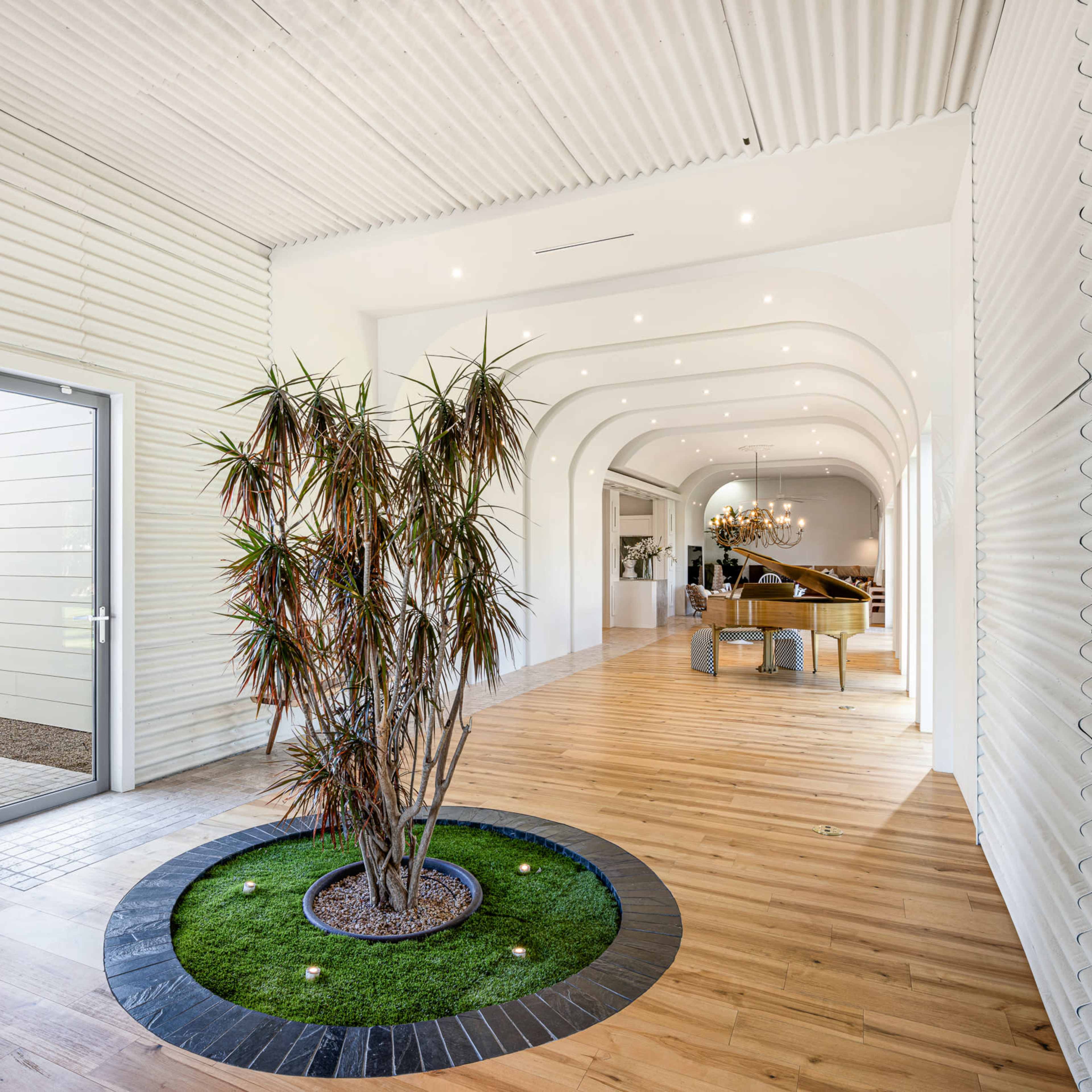 A hallway features a central potted plant surrounded by a circular stone base, leading to an arched entrance that opens into a spacious area with wooden flooring.