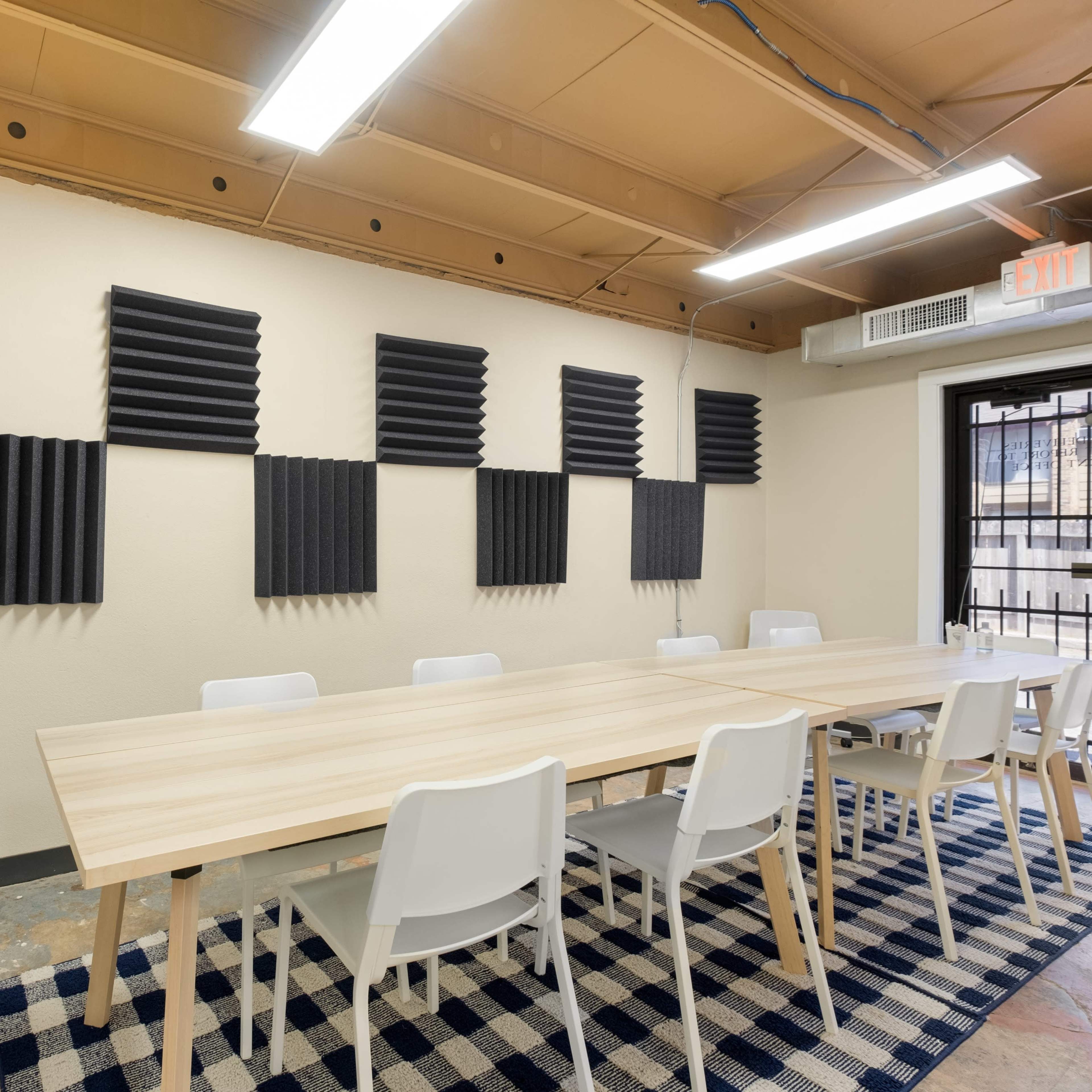 A conference room with a long wooden table, white chairs, acoustic panels on the wall, and a whiteboard.