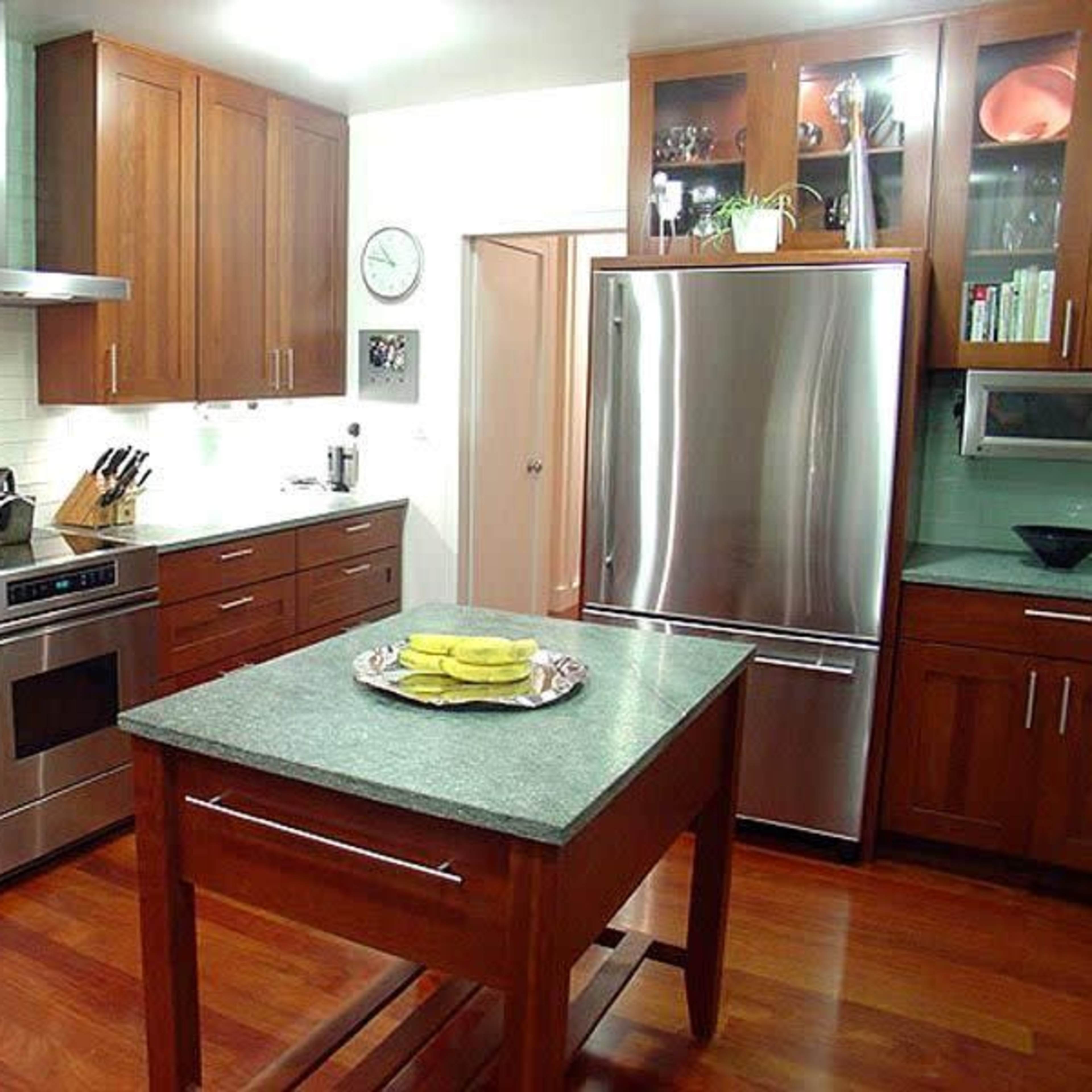 A modern kitchen with wooden cabinets, stainless steel appliances, and a central island with a plate of yellow fruit on it.