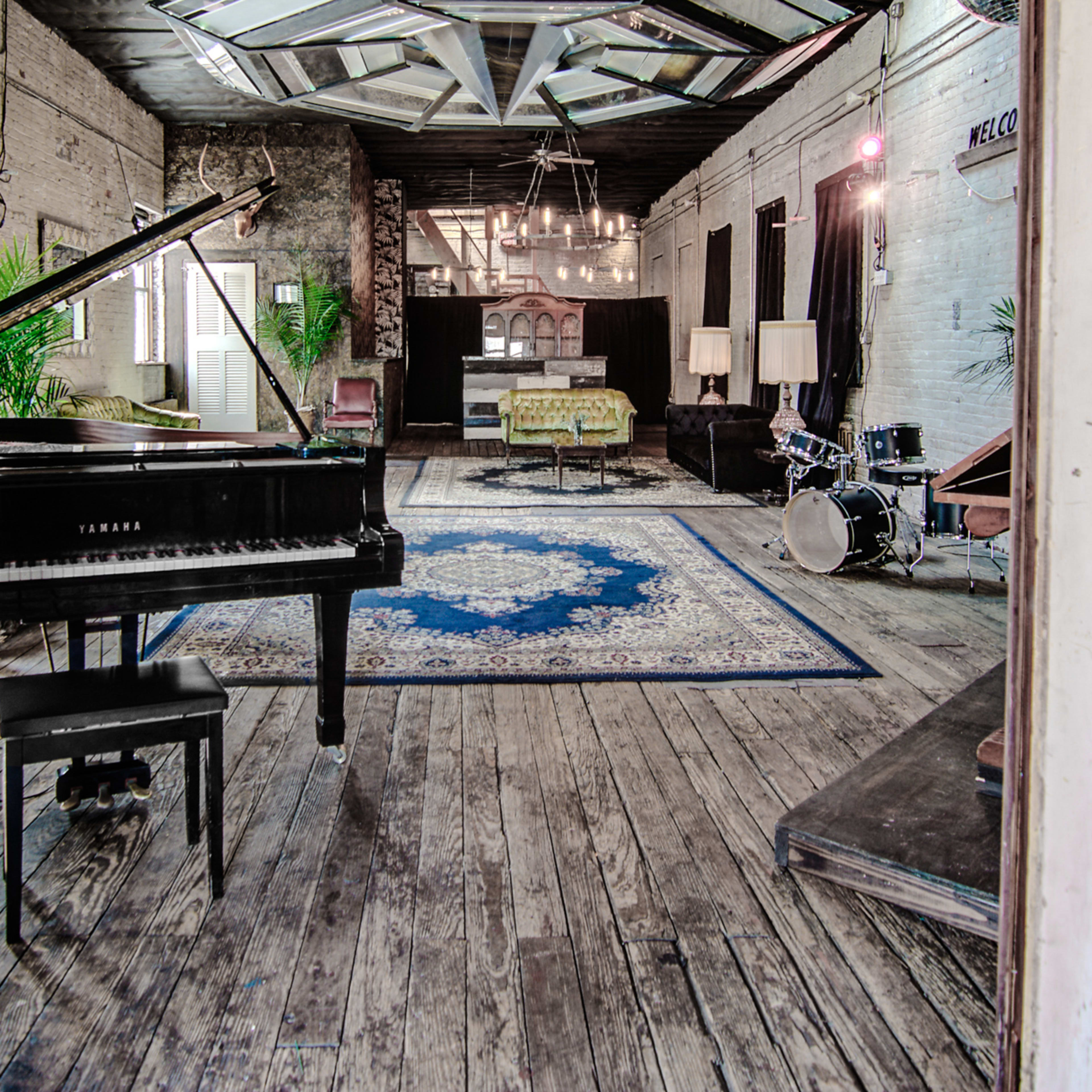 A spacious room with a grand piano, a drum set, and various seating areas on a wooden floor.