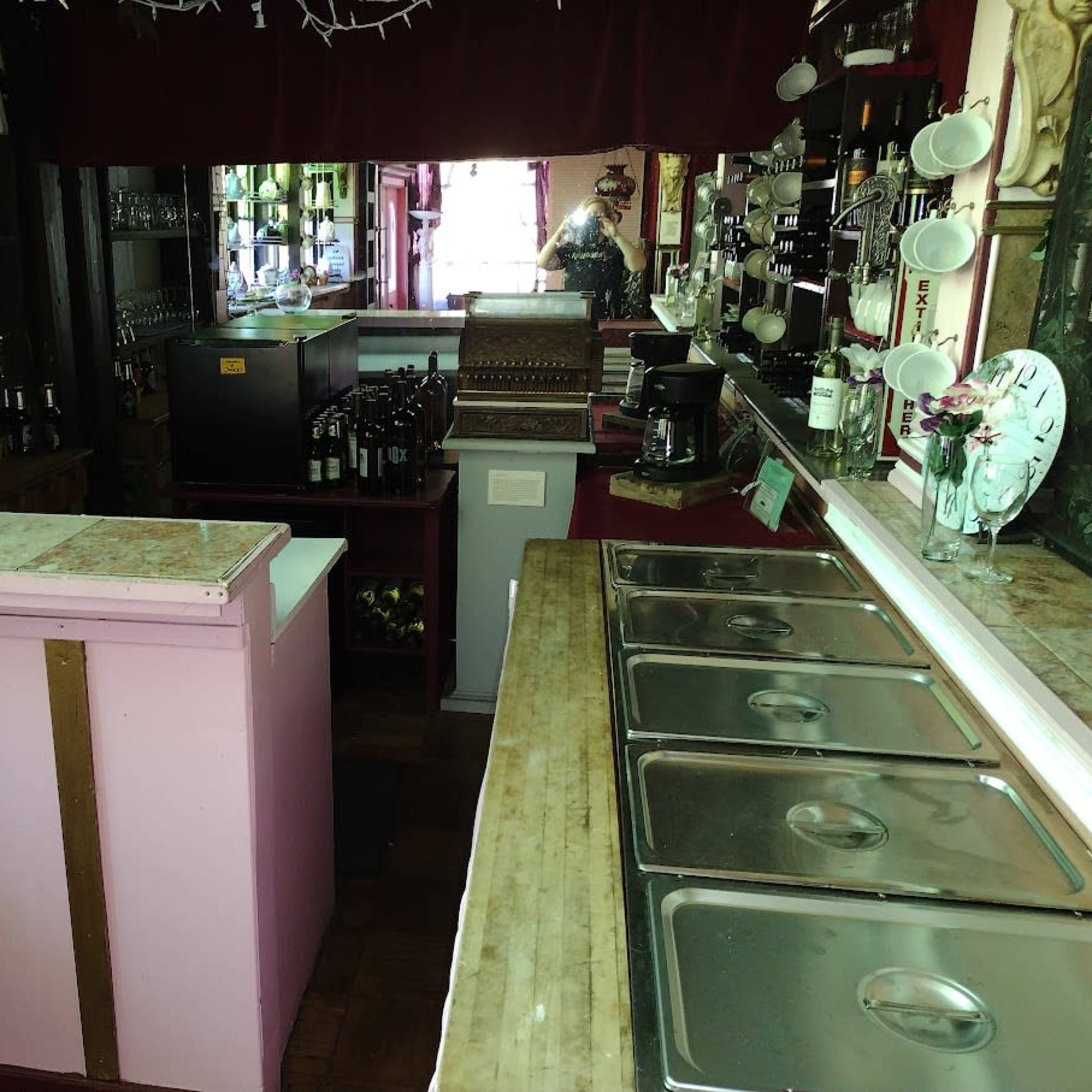 The interior of a small bar with a long counter, shelves filled with bottles, and several sinks lined along the wall.