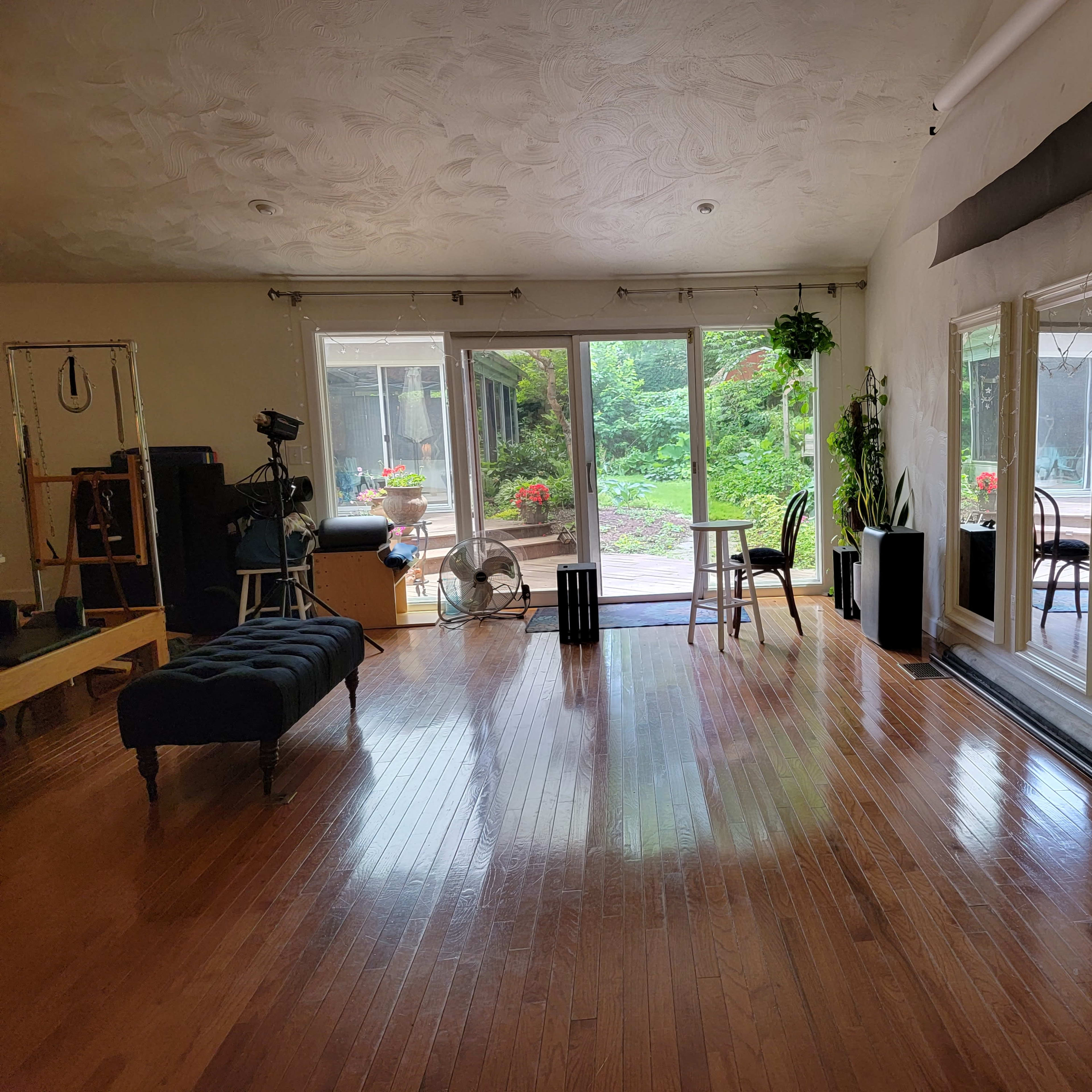 A spacious room with wooden floors, large mirrors on one wall, and a view of a garden through sliding glass doors.