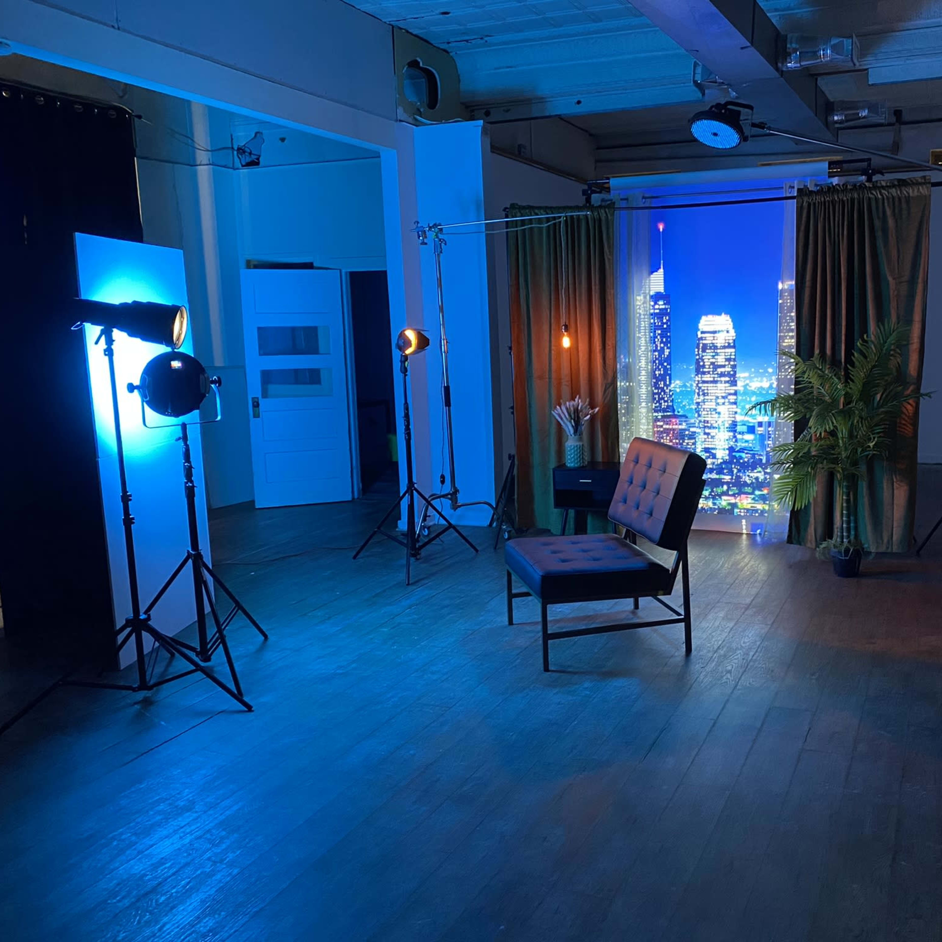 The scene shows a studio setup with a black chair, lighting equipment, and a backdrop featuring a city skyline.