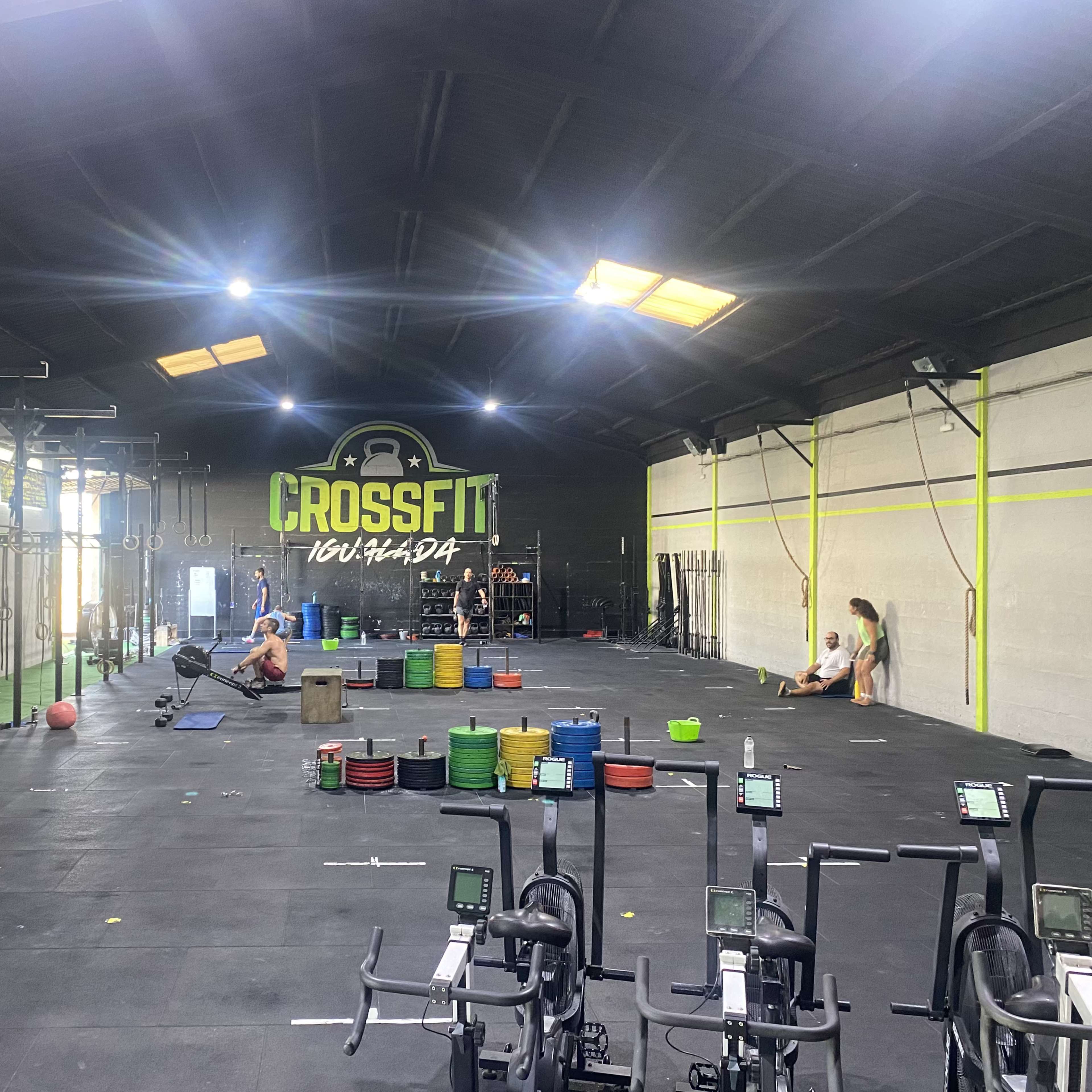 A spacious CrossFit gym with exercise equipment, weightlifting plates arranged on the floor, and individuals engaged in workouts.