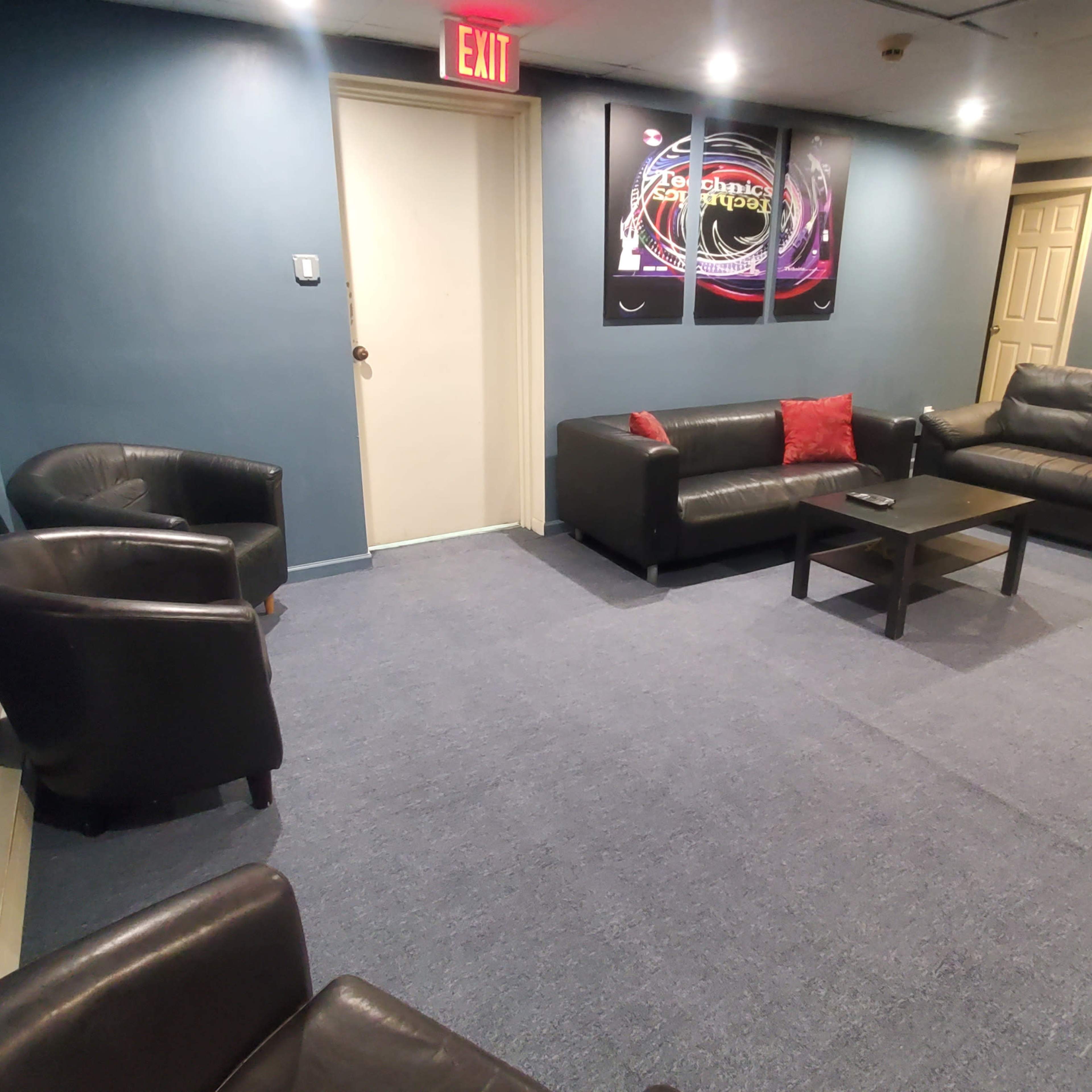 A lounge area with black leather sofas, chairs, a small coffee table, and a wall-mounted decorative piece, all situated on a blue carpet.