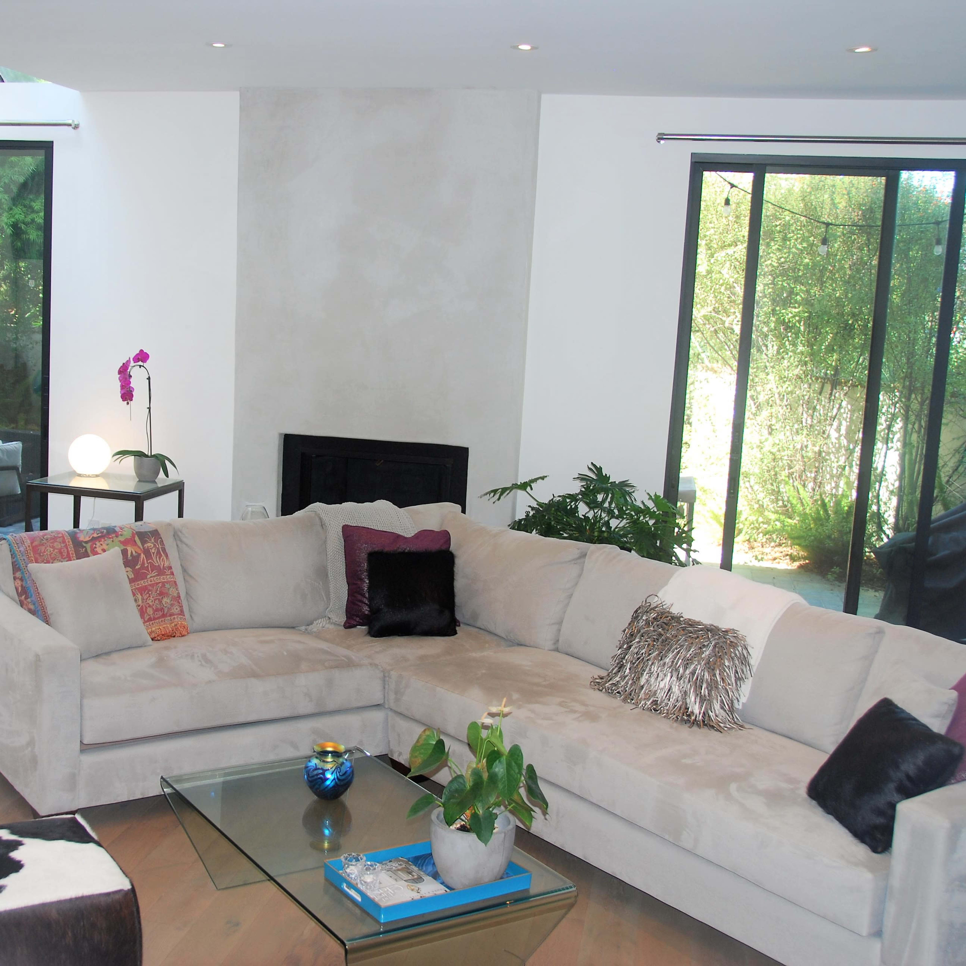 A modern living room featuring a large sectional sofa, a coffee table with a decorative item, and large windows overlooking a green outdoor area.