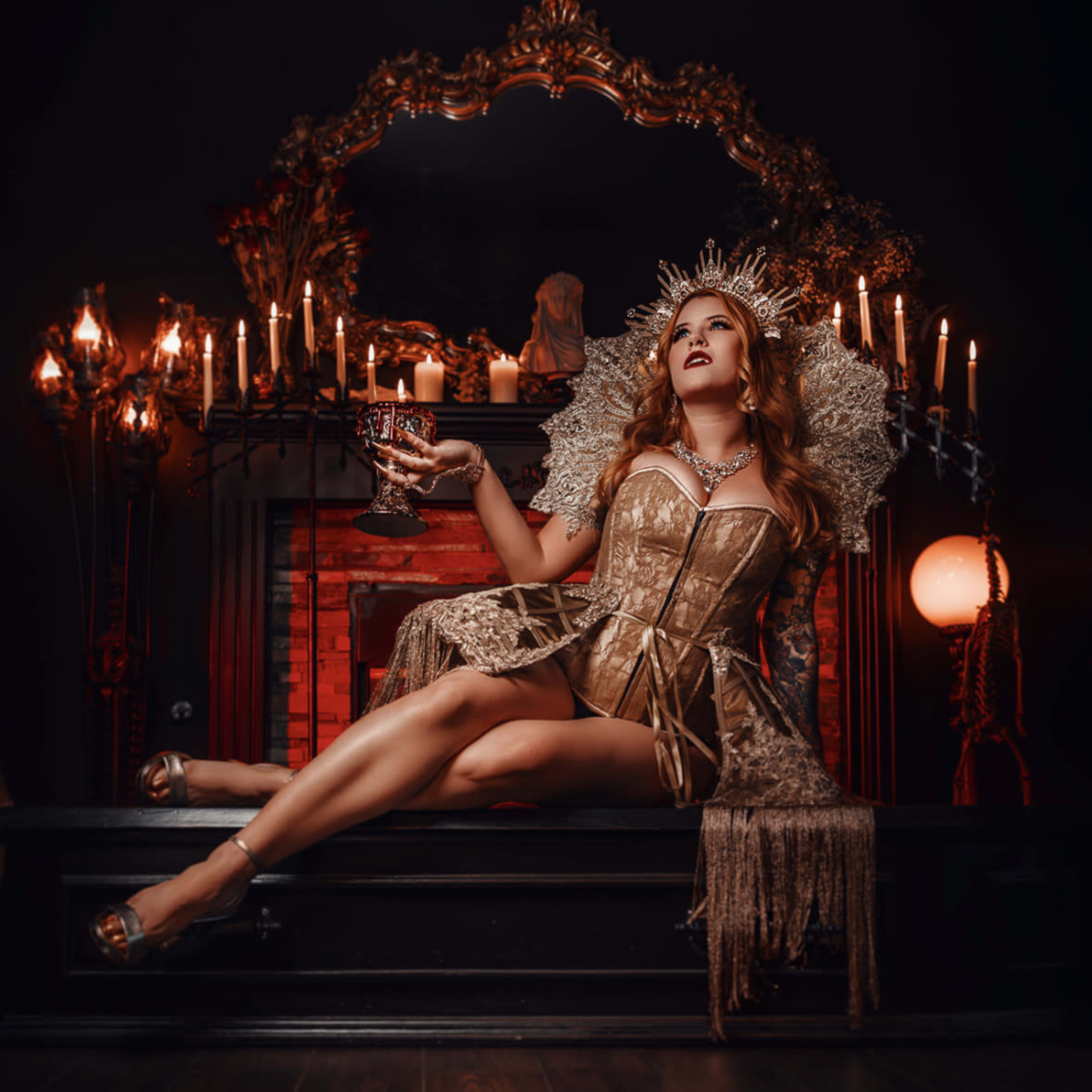 A woman in a gold corset sits on an ornate throne surrounded by candles, holding a goblet in a dark, elegantly decorated room.