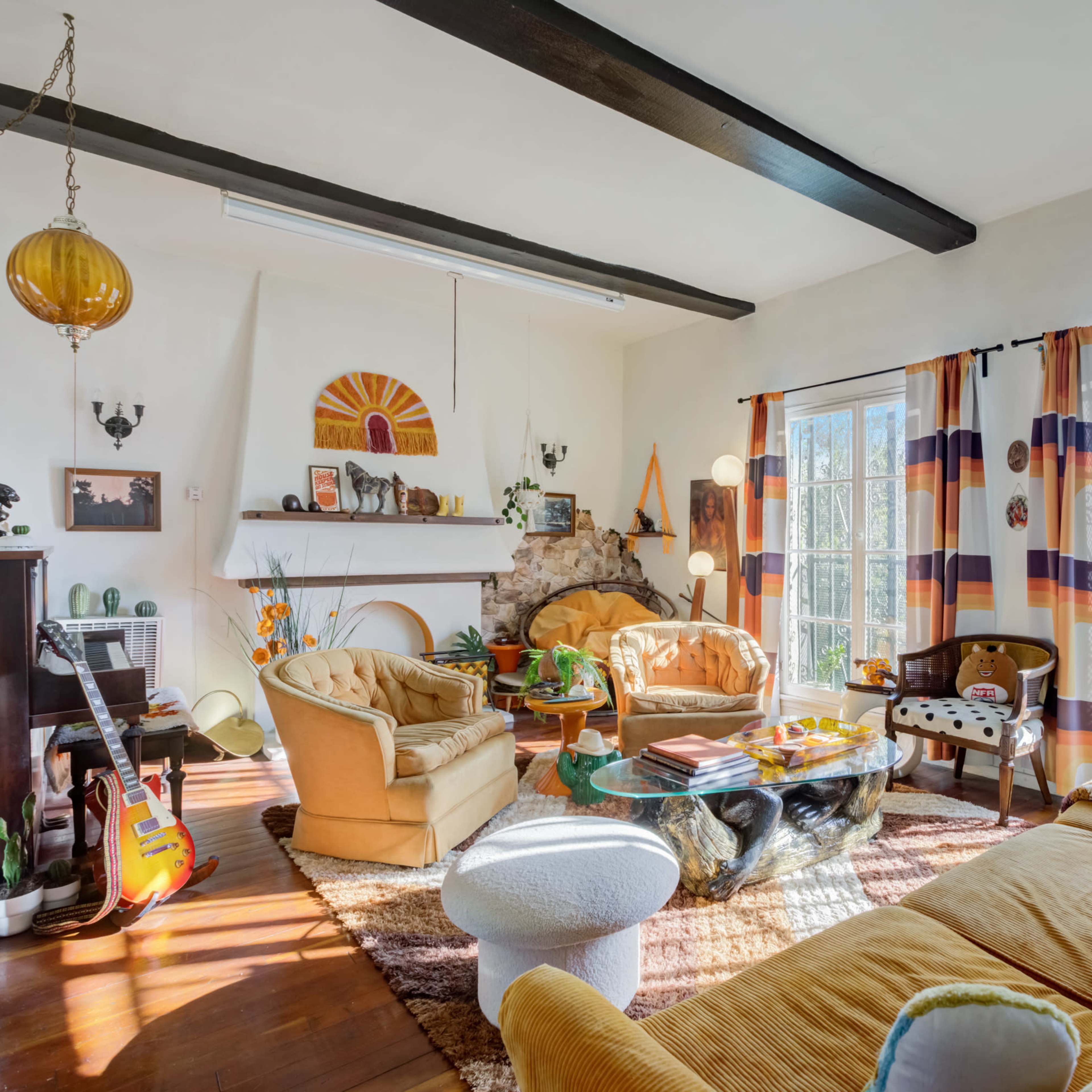 The living room features two armchairs, a sofa, a coffee table, and large windows adorned with patterned curtains, along with a fireplace and various decorative items.