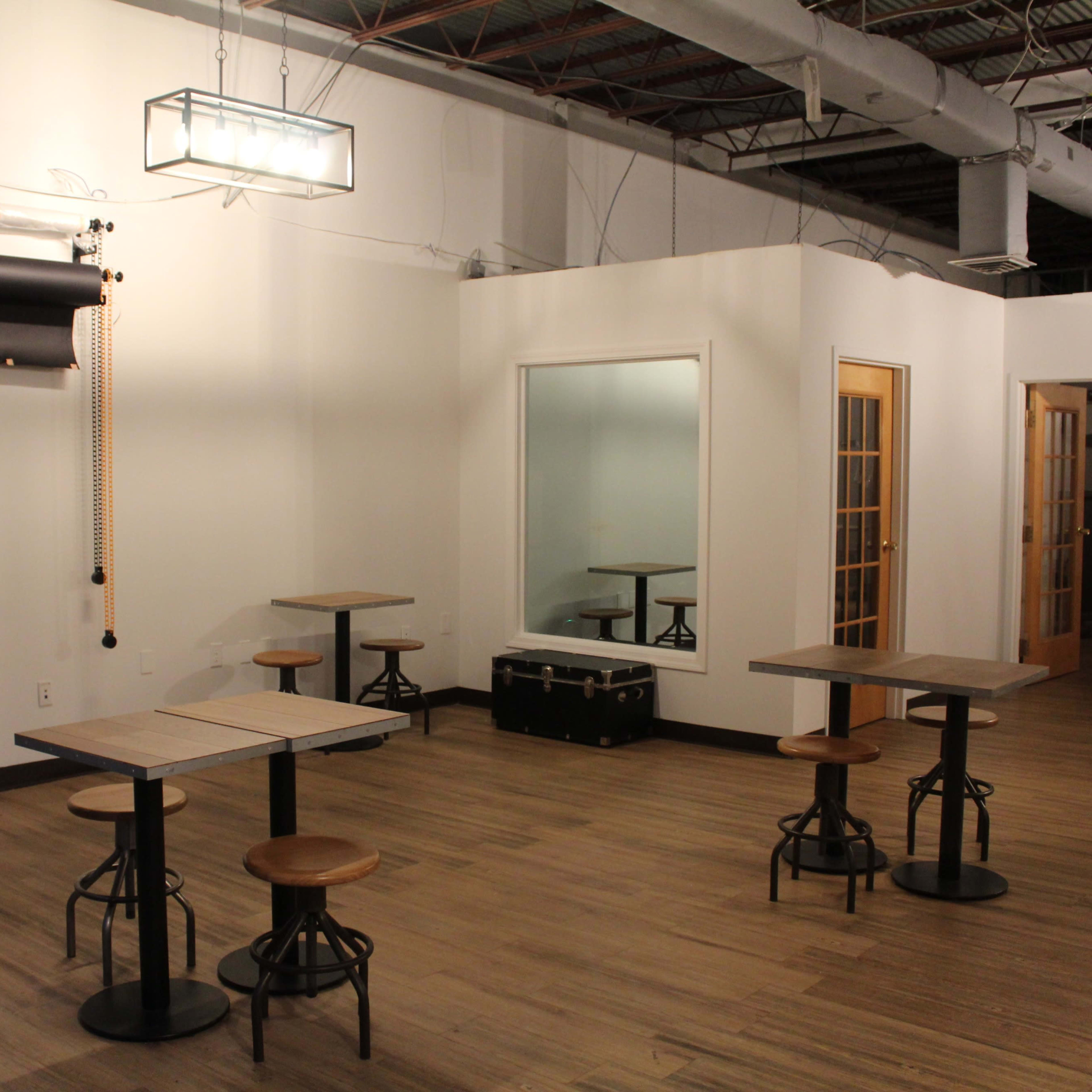 A sparsely furnished room with wooden tables and stools, a large mirror, and a ceiling light fixture.