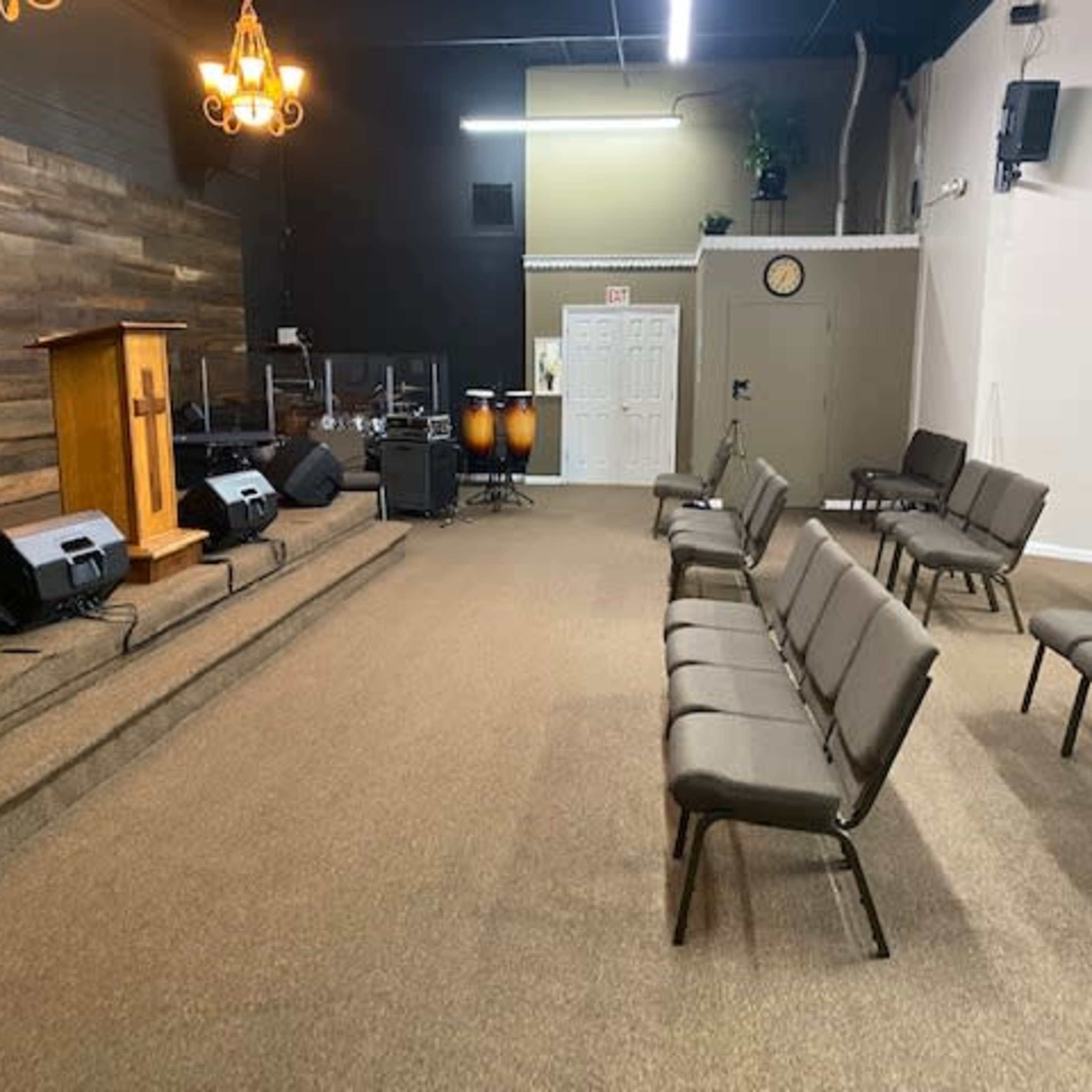 A church interior with a wooden podium, musical instruments, and rows of chairs arranged in a carpeted space.