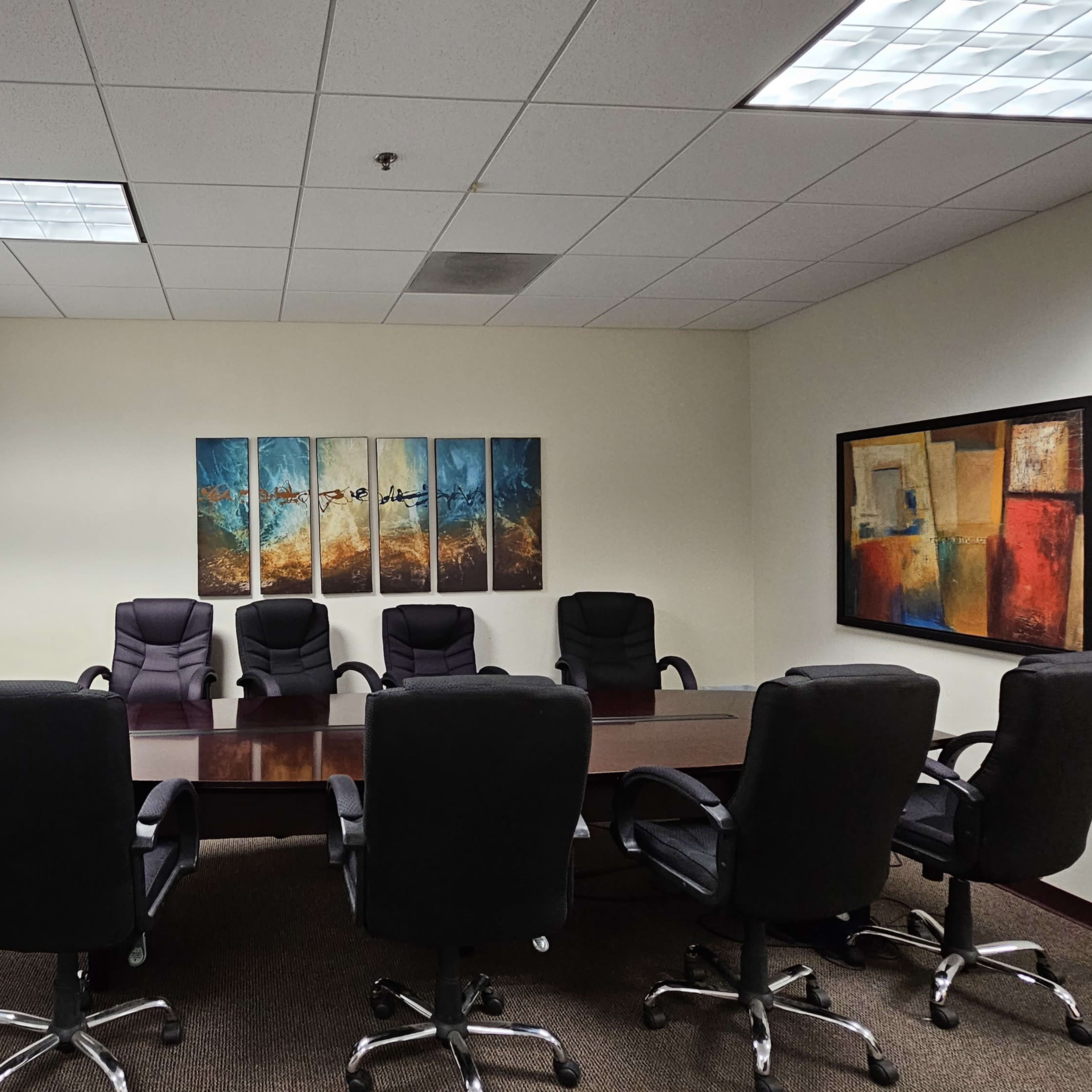 A conference room with a large wooden table surrounded by black chairs, and artwork displayed on the walls.