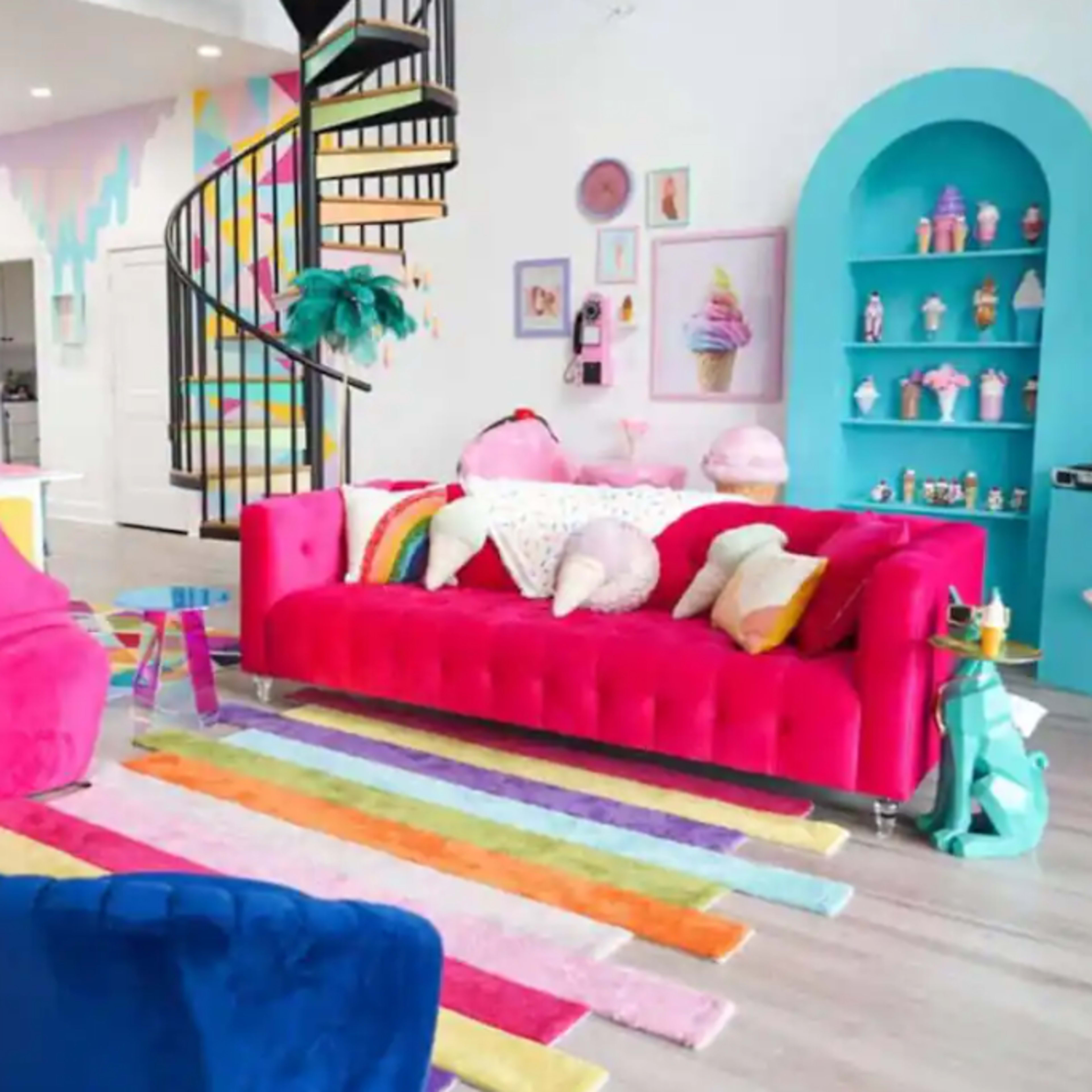 A brightly decorated living room with pink sofas, a colorful rug, and a spiral staircase leading to an upper level.