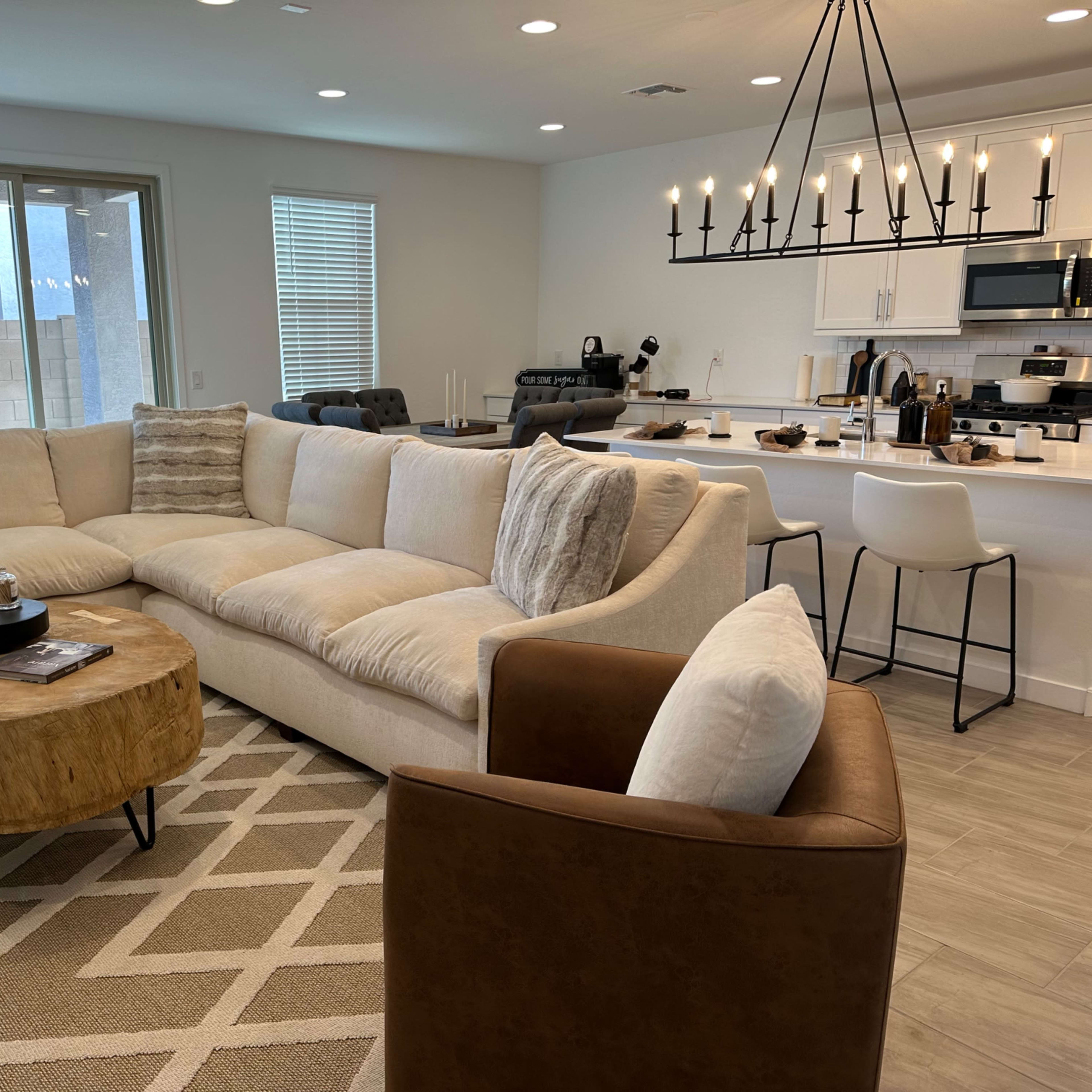 A modern living room with a large sectional sofa, a round wooden coffee table, and a kitchen area visible in the background.