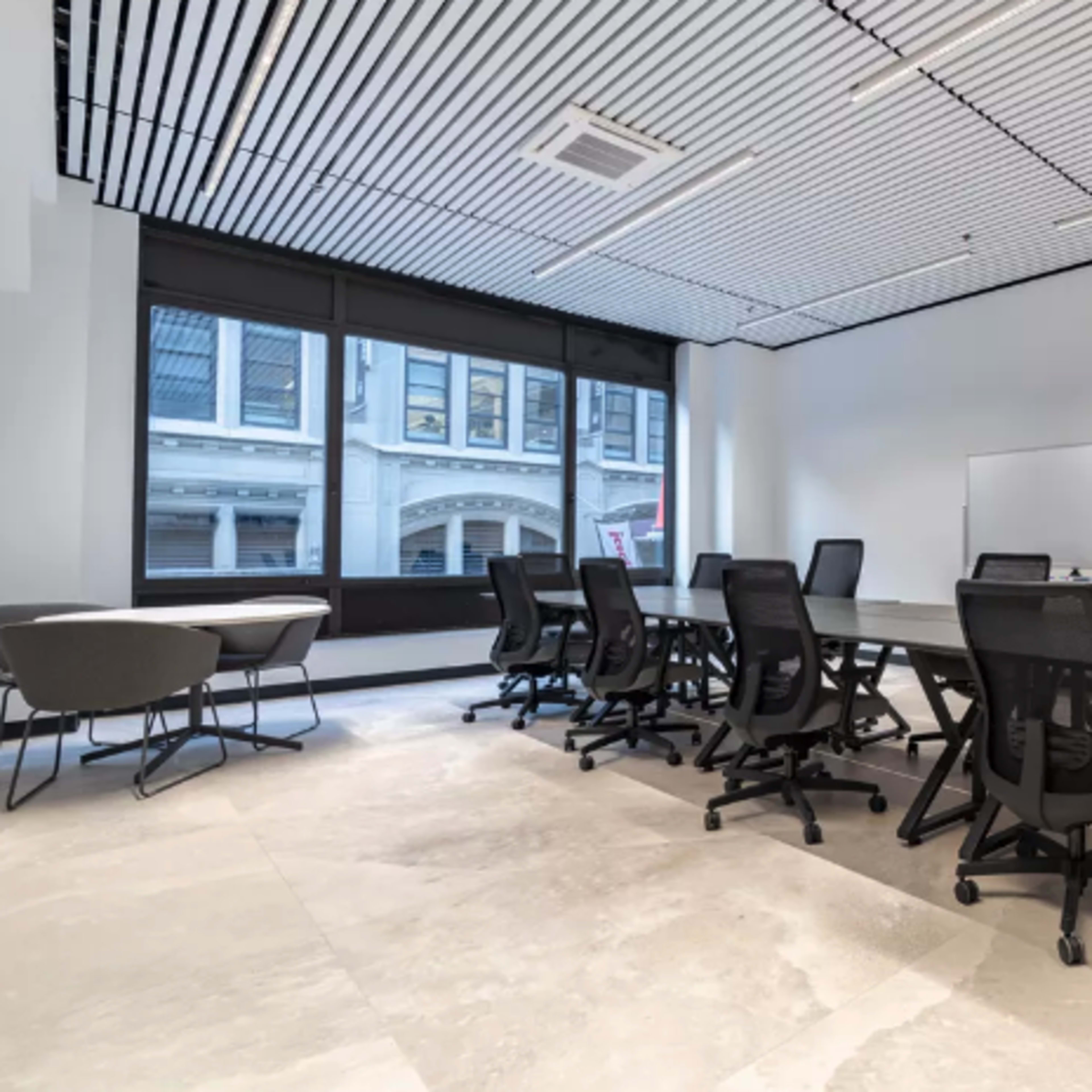 A modern conference room features a long glass table surrounded by ergonomic chairs, with large windows providing natural light.
