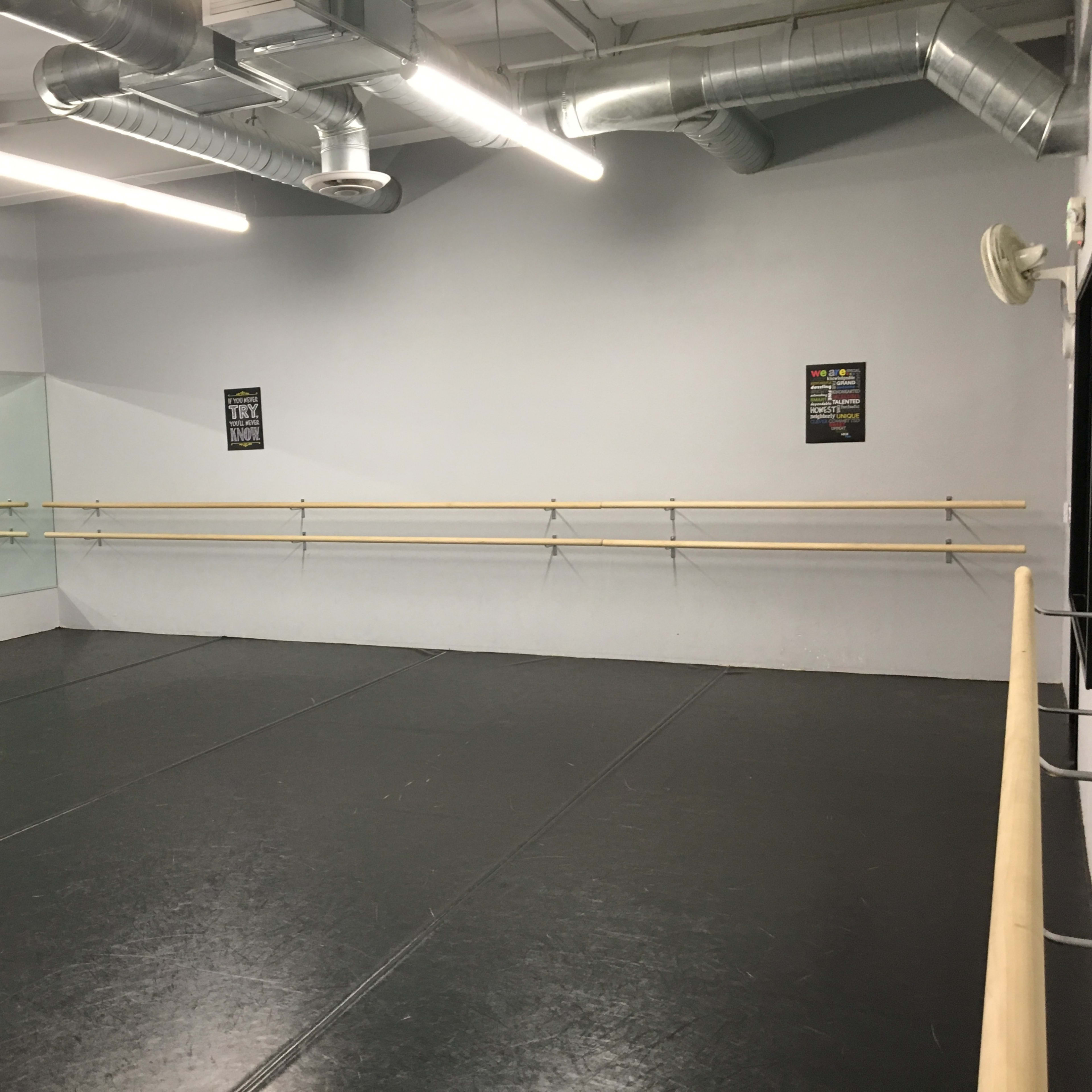 A spacious dance studio with a mirrored wall and wooden ballet bars along the perimeter.