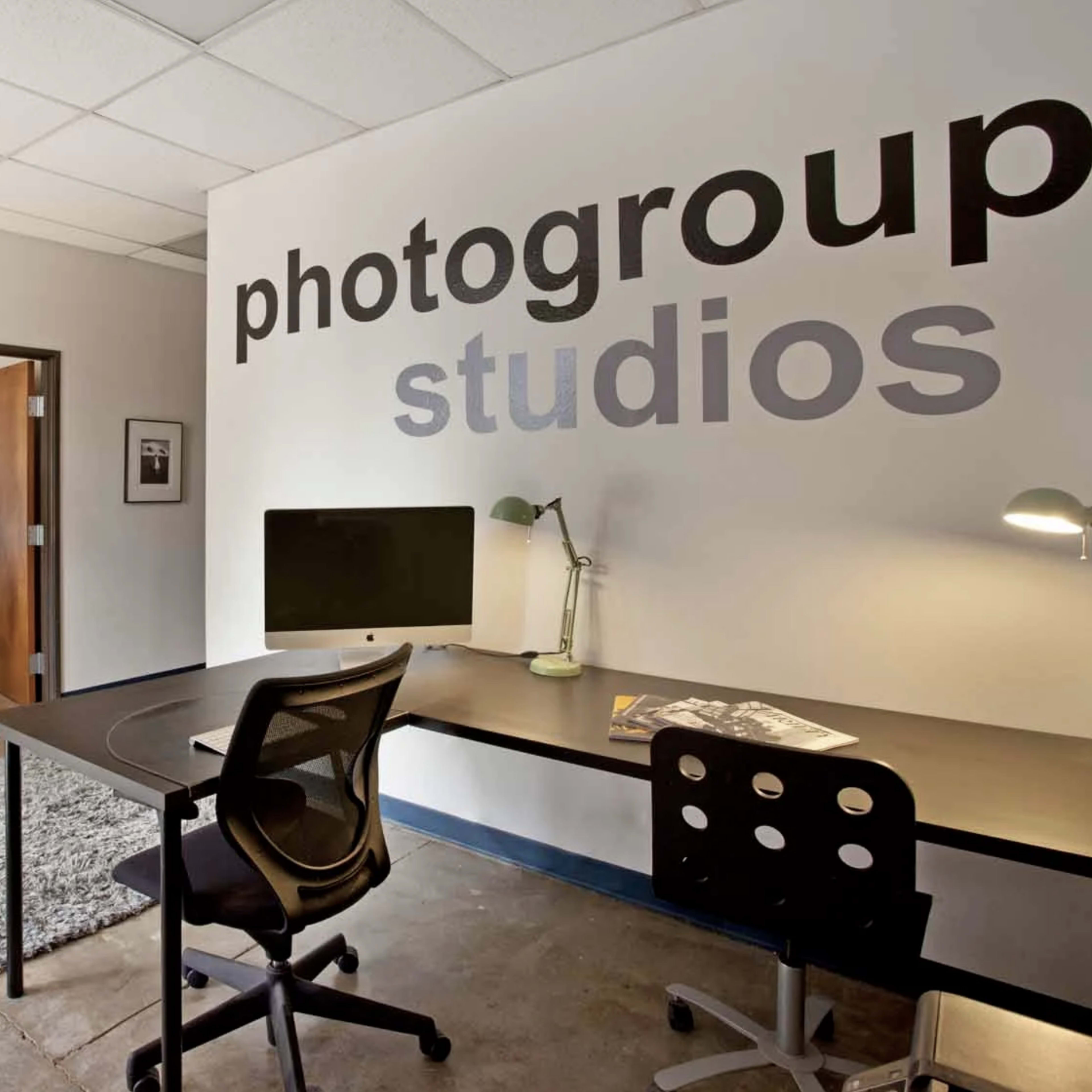 A modern office space featuring a workspace with a desk, chair, and computer, alongside a seating area with a gray couch and a floor lamp.