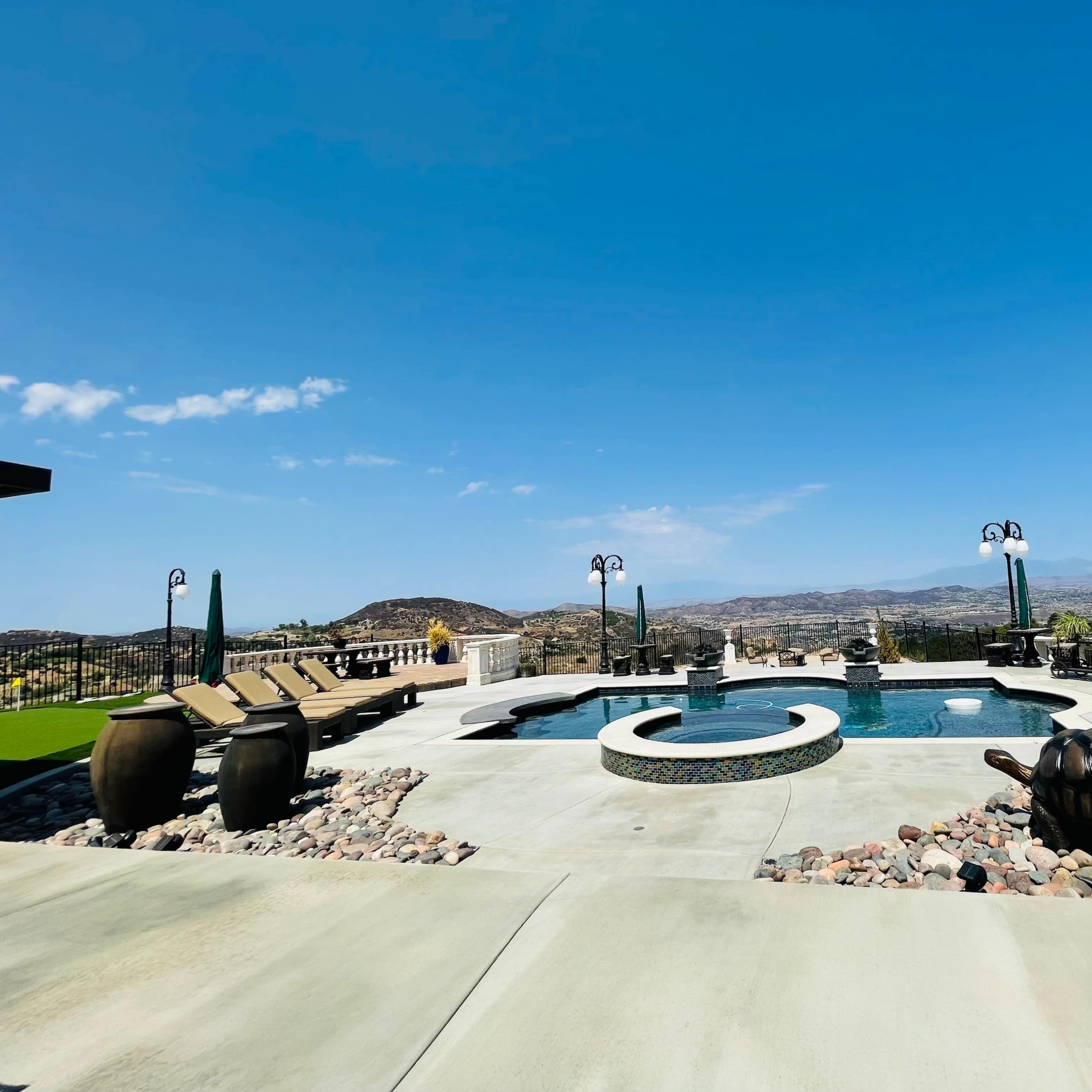 A spacious outdoor area featuring a swimming pool, lounge chairs, and a panoramic view of distant hills under a clear blue sky.