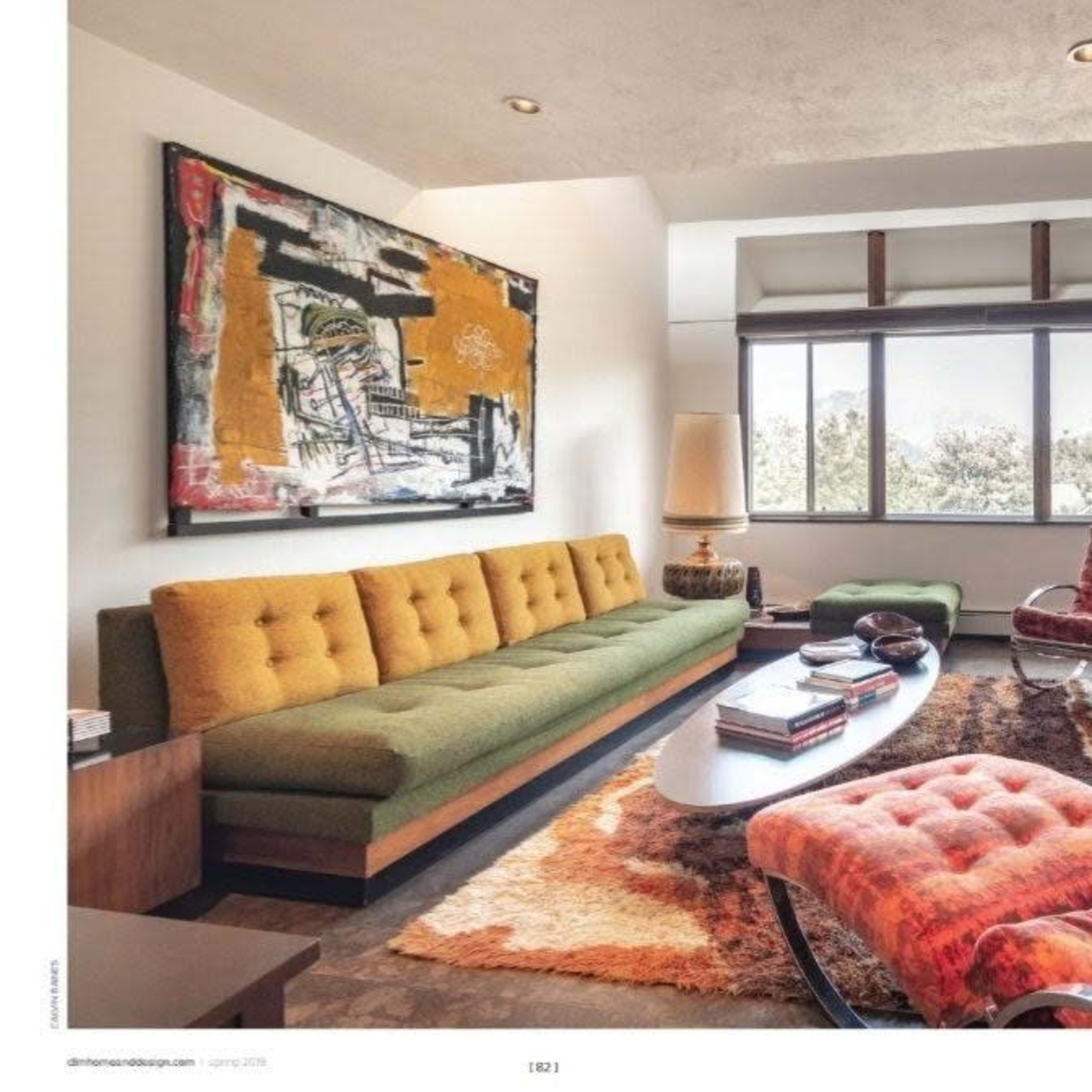 A modern living room featuring a green and orange sectional sofa, a large abstract painting on the wall, a round coffee table, and a rug on the floor.