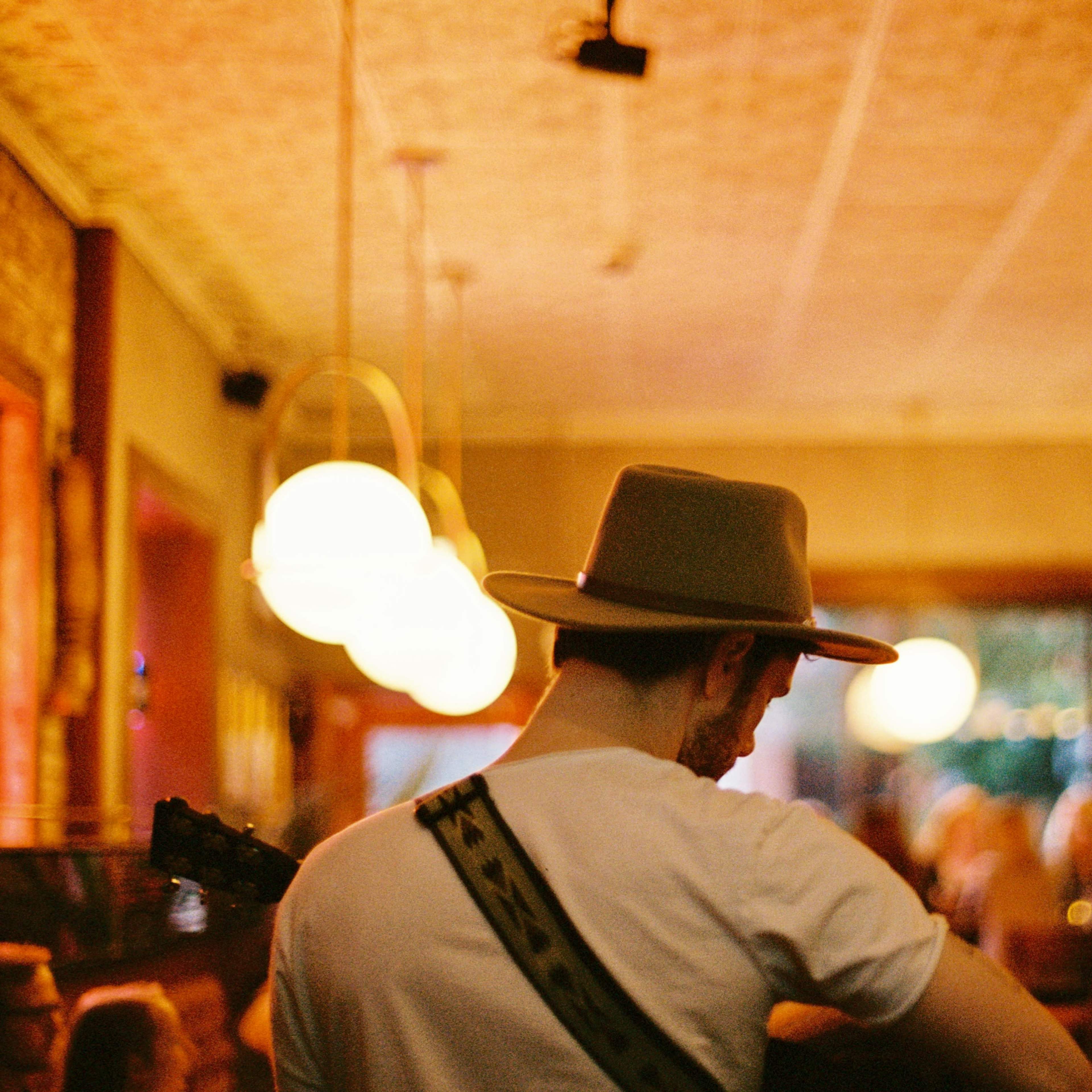 A musician wearing a hat plays guitar in a dimly lit restaurant filled with patrons.