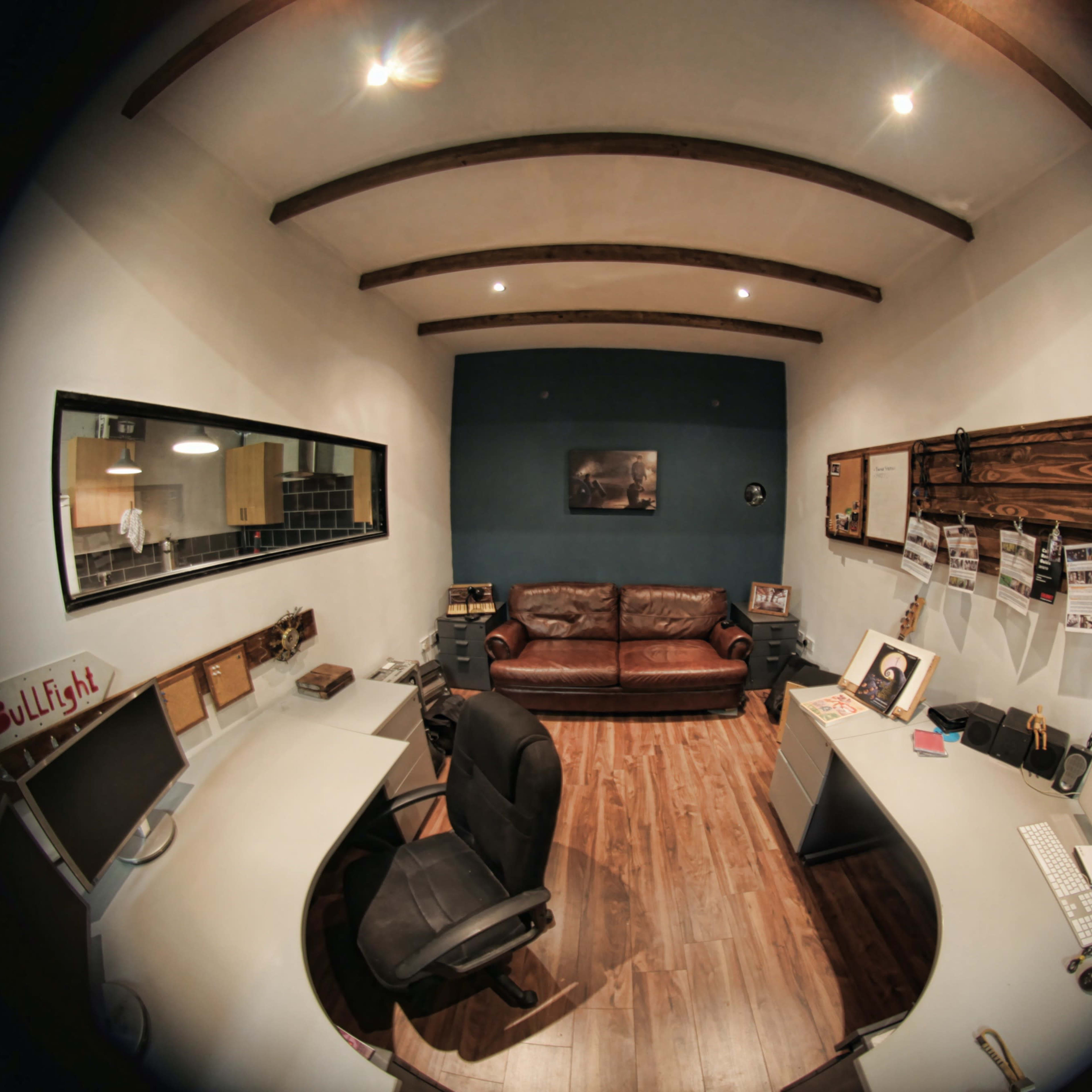 A small office space featuring a brown leather sofa, two workstations with computers, and wooden beams on the ceiling.