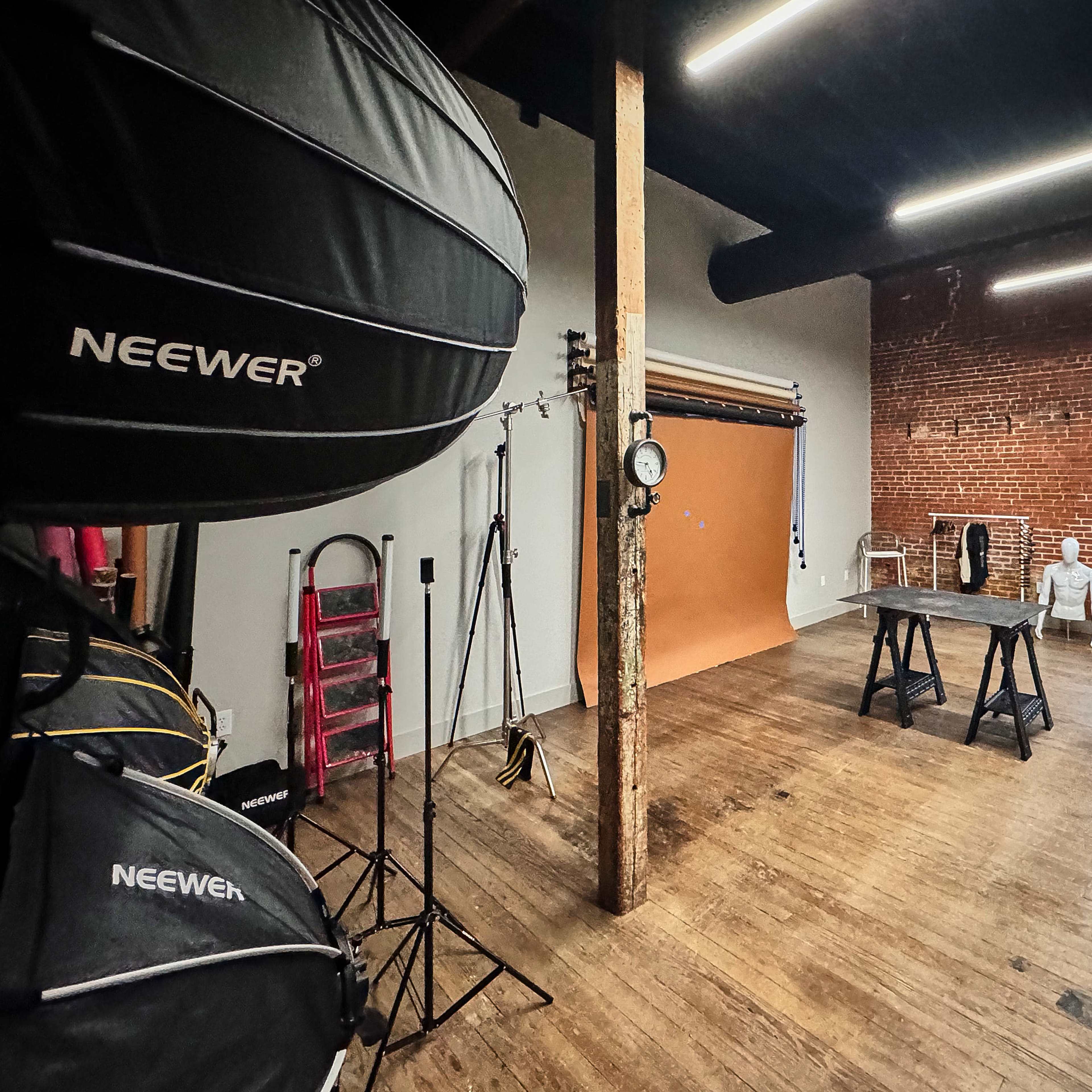 A photo studio featuring brick walls, wooden floors, a backdrop, lighting equipment, and a couch.
