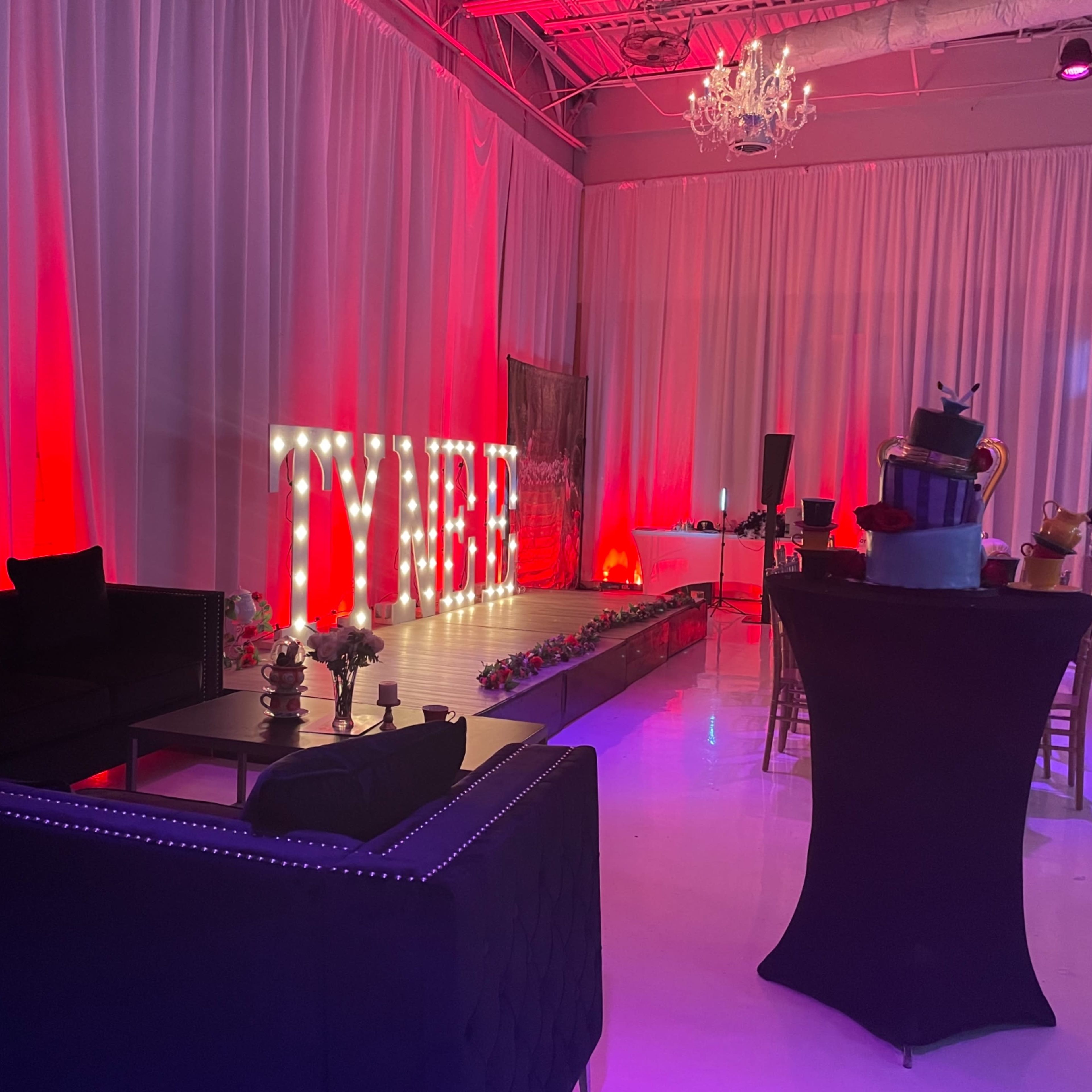 A decorated event space featuring a marquee sign that spells "TYRE," with plush seating and a birthday cake on a table.