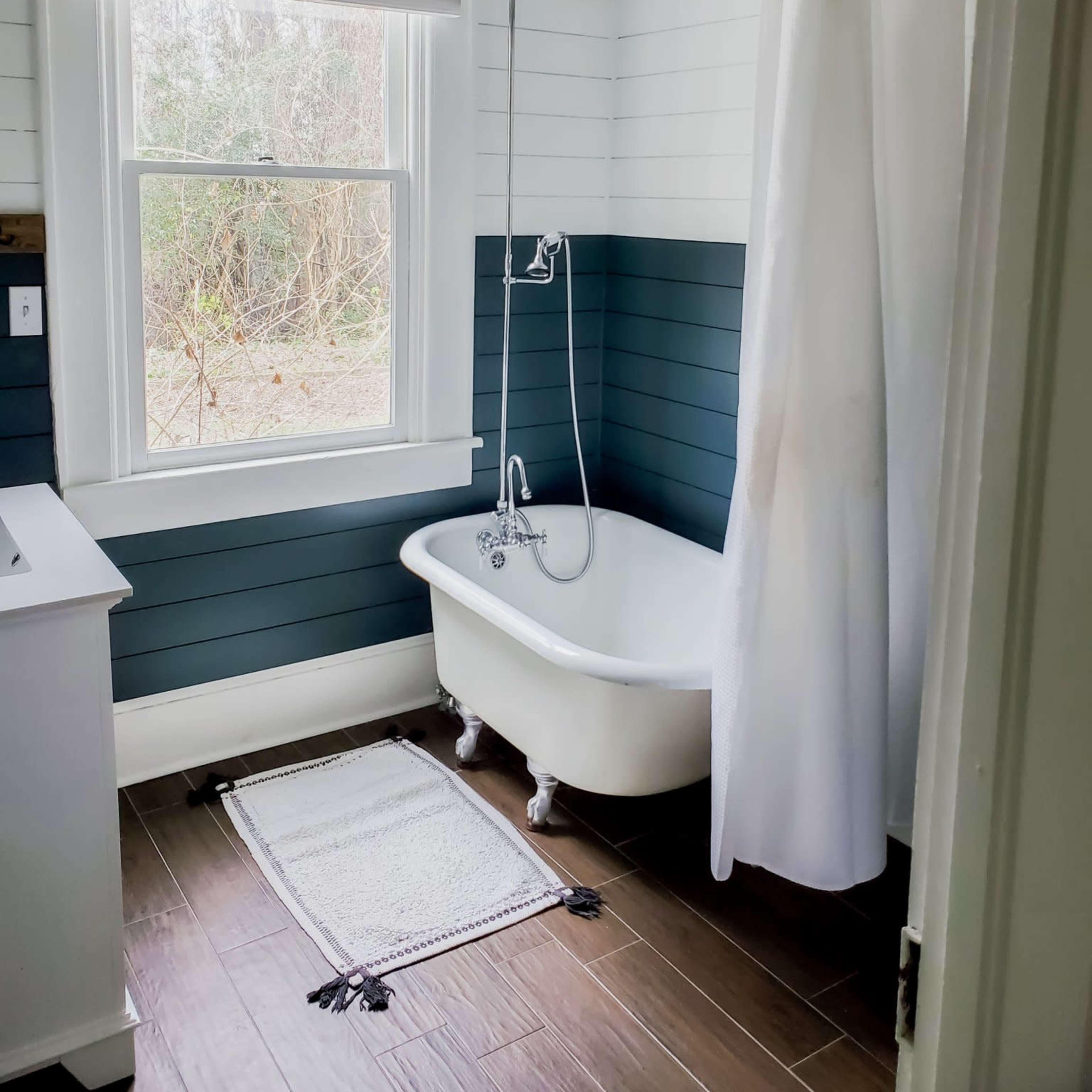A bathroom with a freestanding bathtub, a shower curtain, and a window overlooking a wooded area.