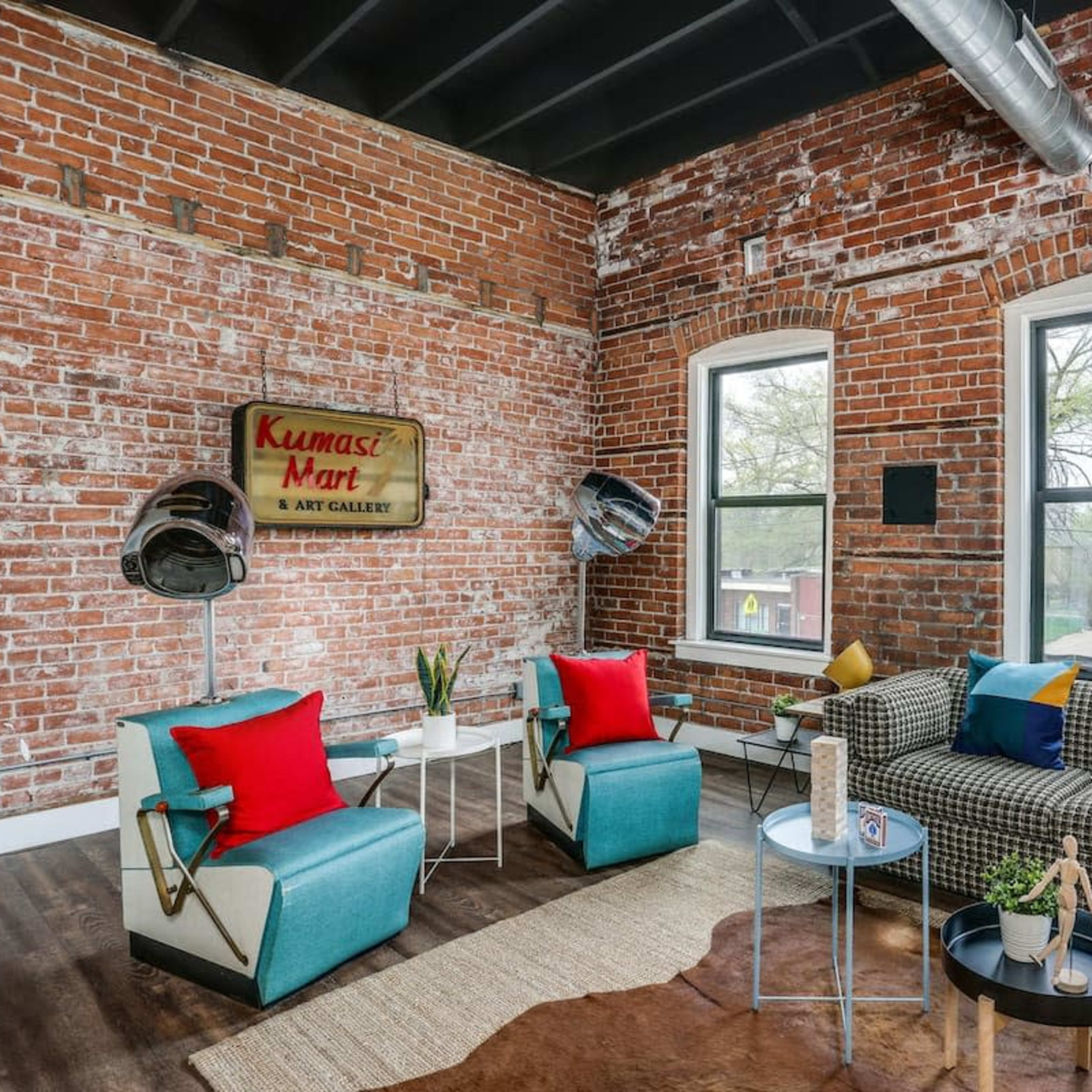 A stylish interior with exposed brick walls, two large windows, a patterned sofa, and modern decor including a coffee table and floor lamps.