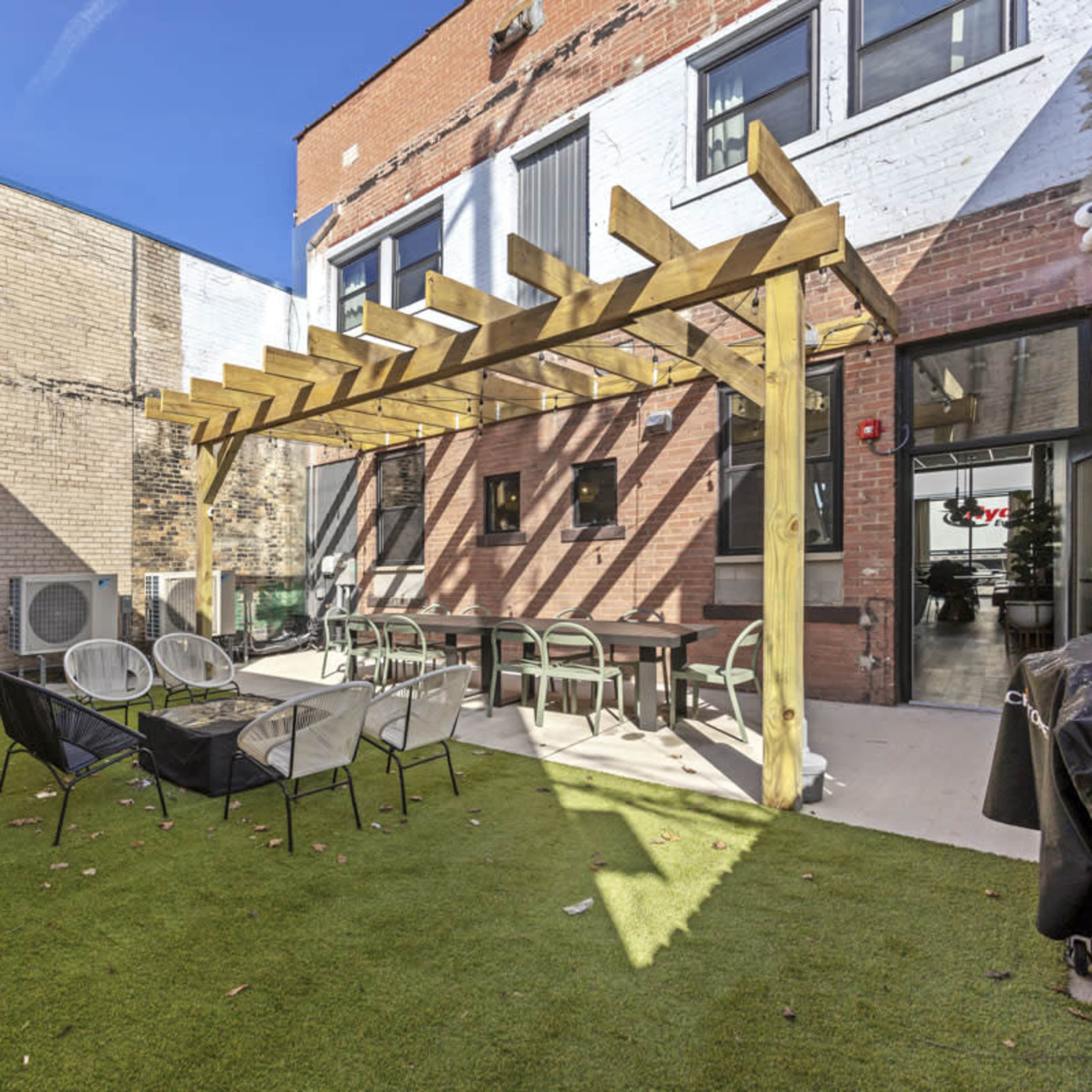 A courtyard with a wooden pergola, surrounded by brick walls, featuring outdoor furniture and artificial grass.