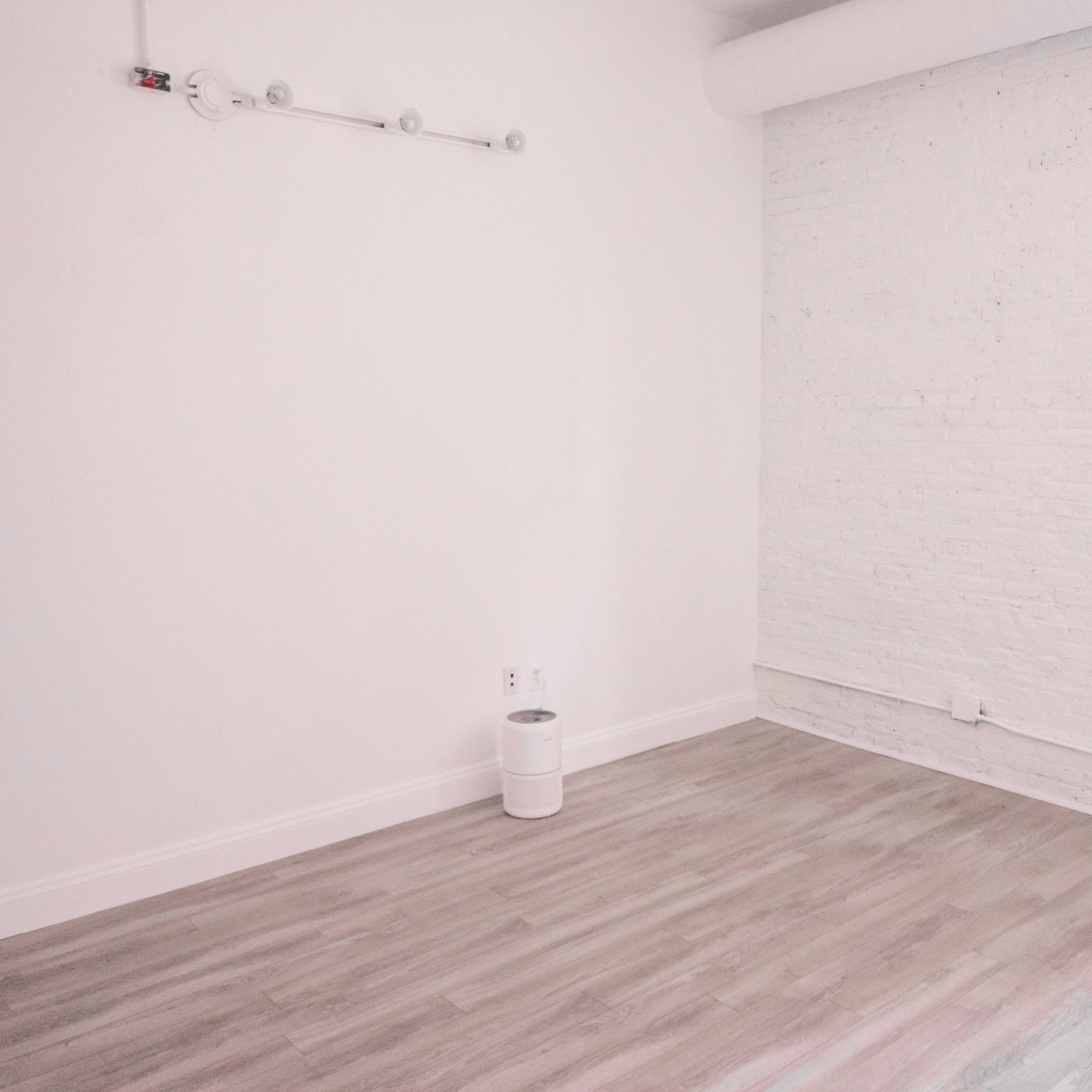 A sparsely furnished room with white brick walls and light wooden flooring.