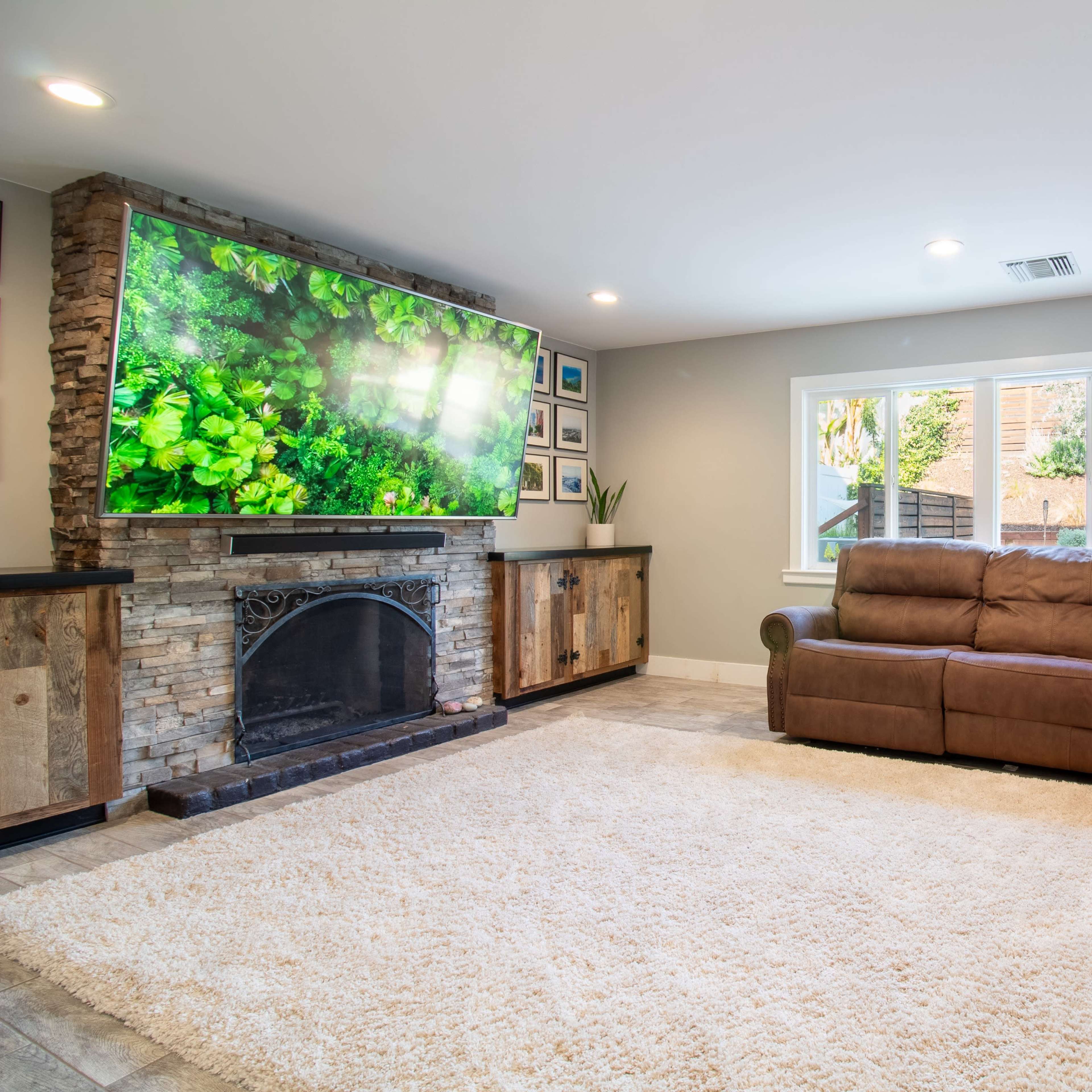 The living room features a large sectional sofa, a stone fireplace, and a wall-mounted television displaying a nature scene, with a plush rug covering the floor.