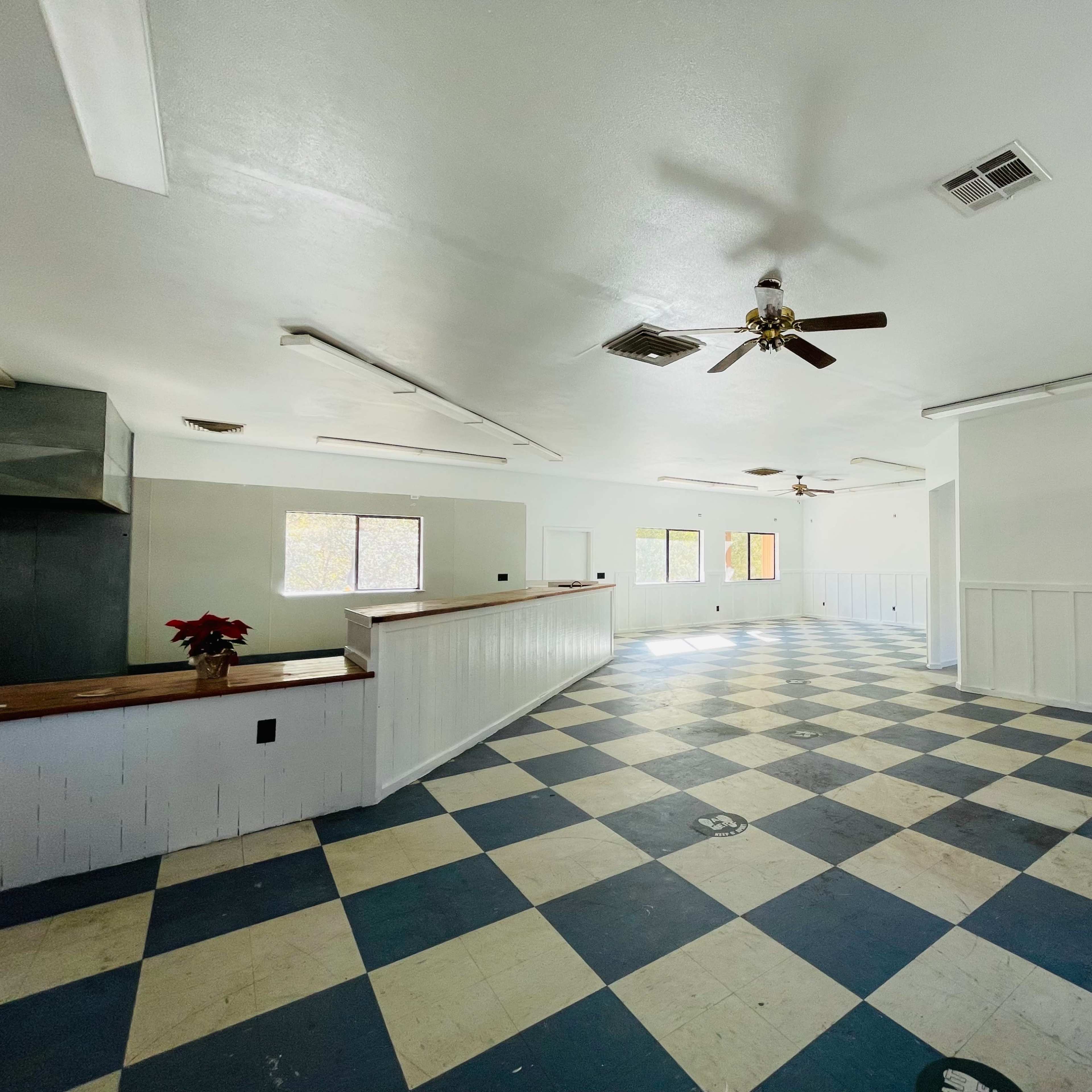 An empty room with a checkerboard blue and white floor, ceiling fans, and several windows allowing natural light.