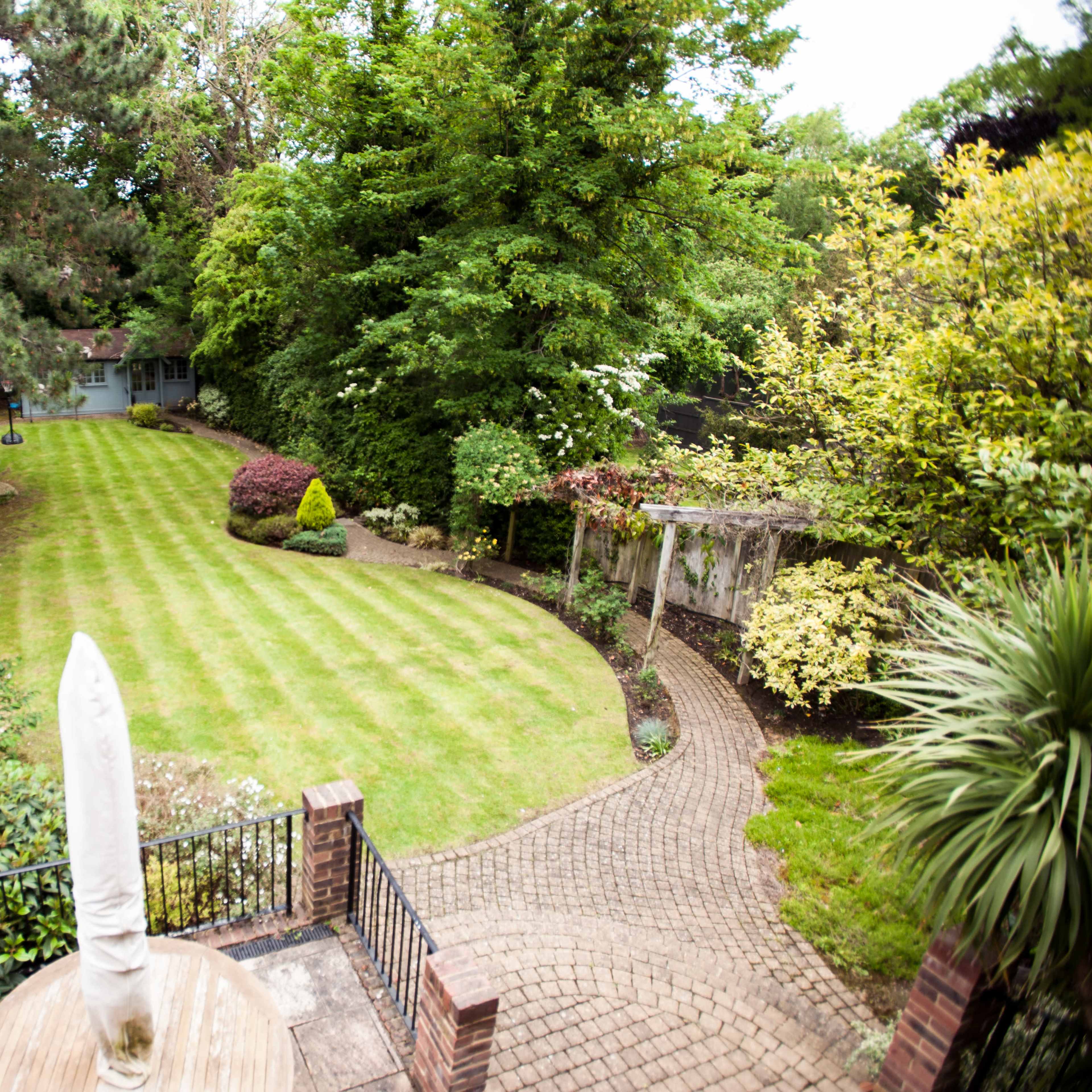 A well-maintained garden with neatly striped grass, surrounded by various trees and shrubs, complemented by a stone path leading to a secluded area.