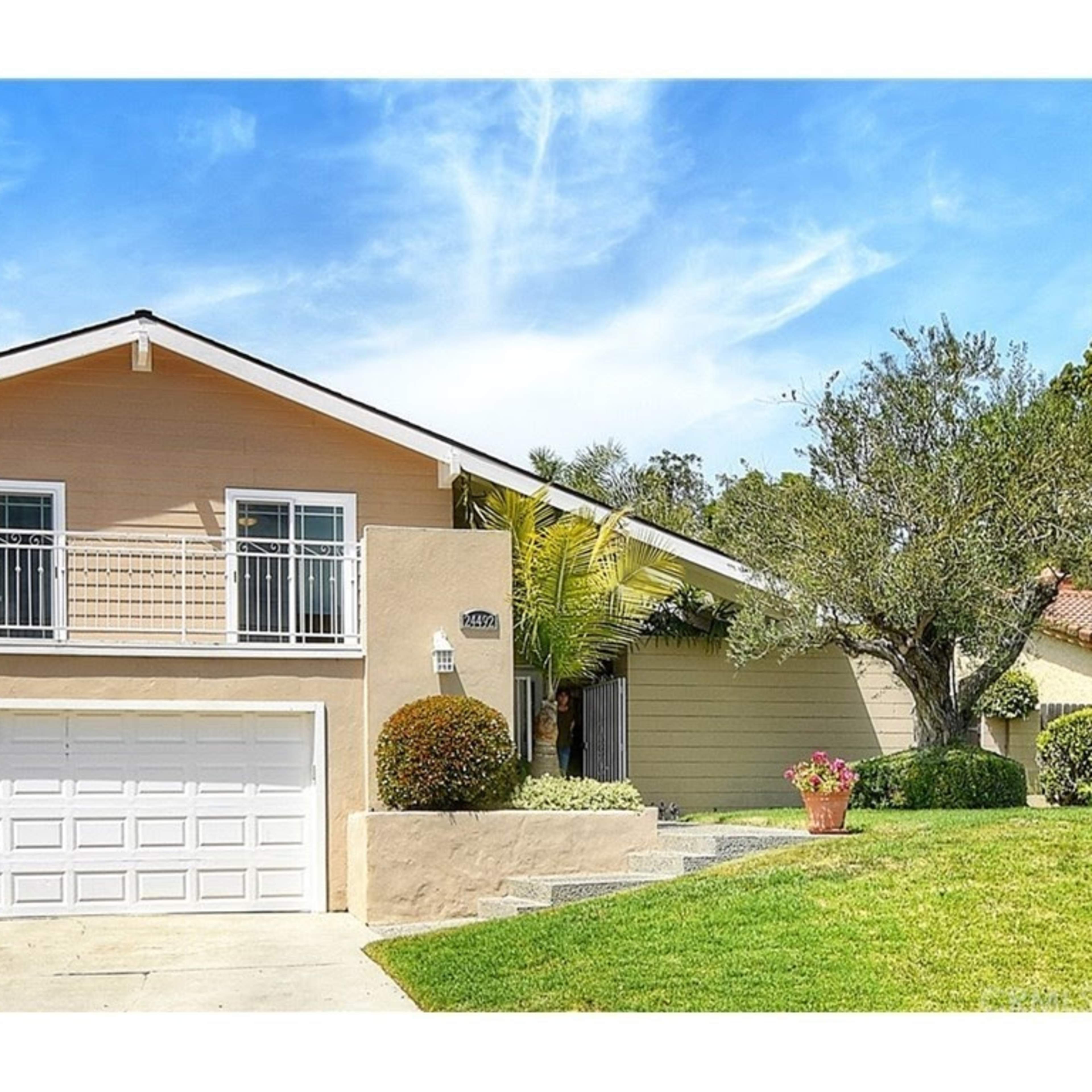 A two-story residential house with a garage, a balcony on the upper floor, and a well-maintained front lawn.