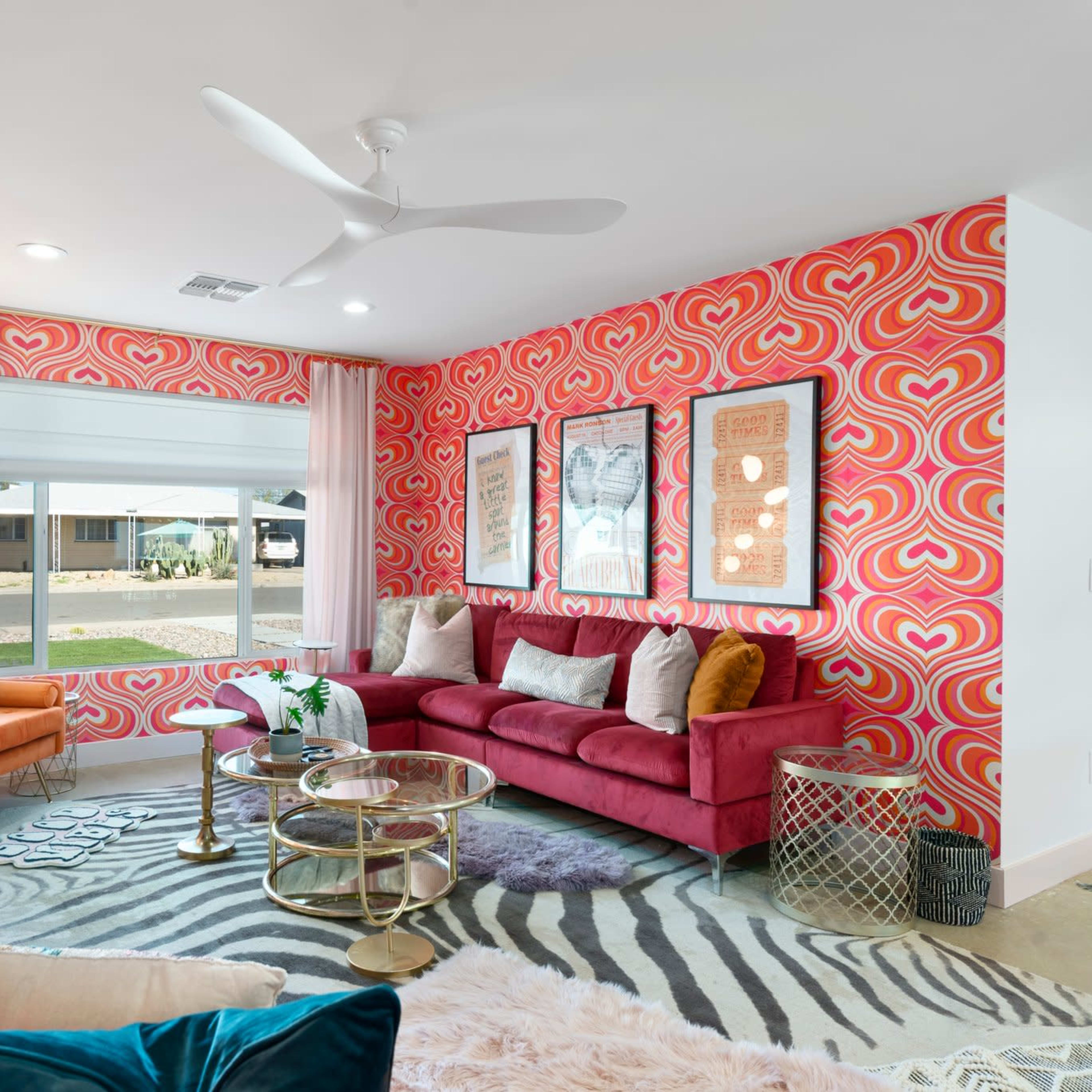 The living room features a vibrant pink heart-patterned wall, a red sofa, and a mix of colorful decor elements, including a zebra-striped rug and modern furniture.