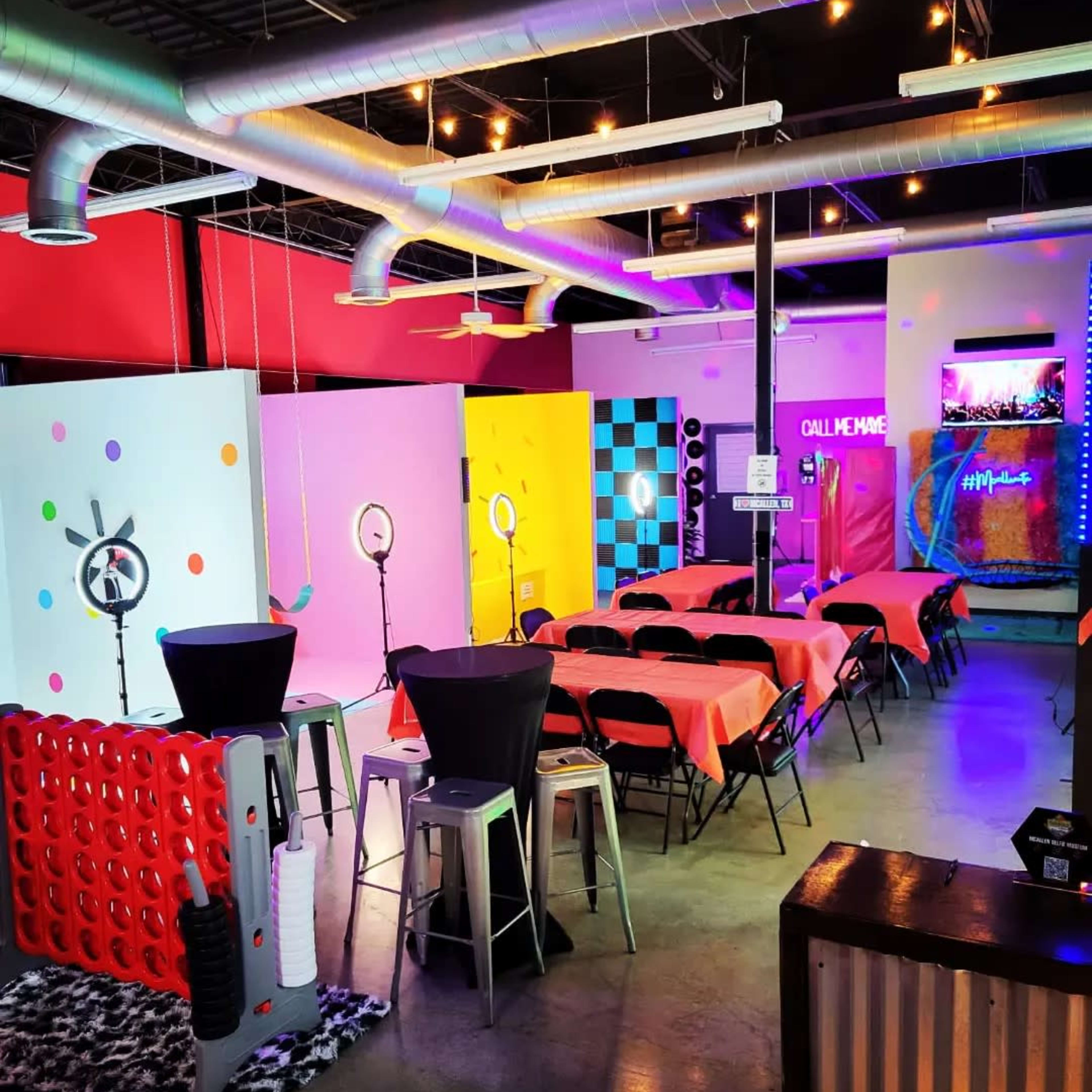 A brightly colored event space with tables covered in orange cloth, decorative walls, and various photo booth setups.