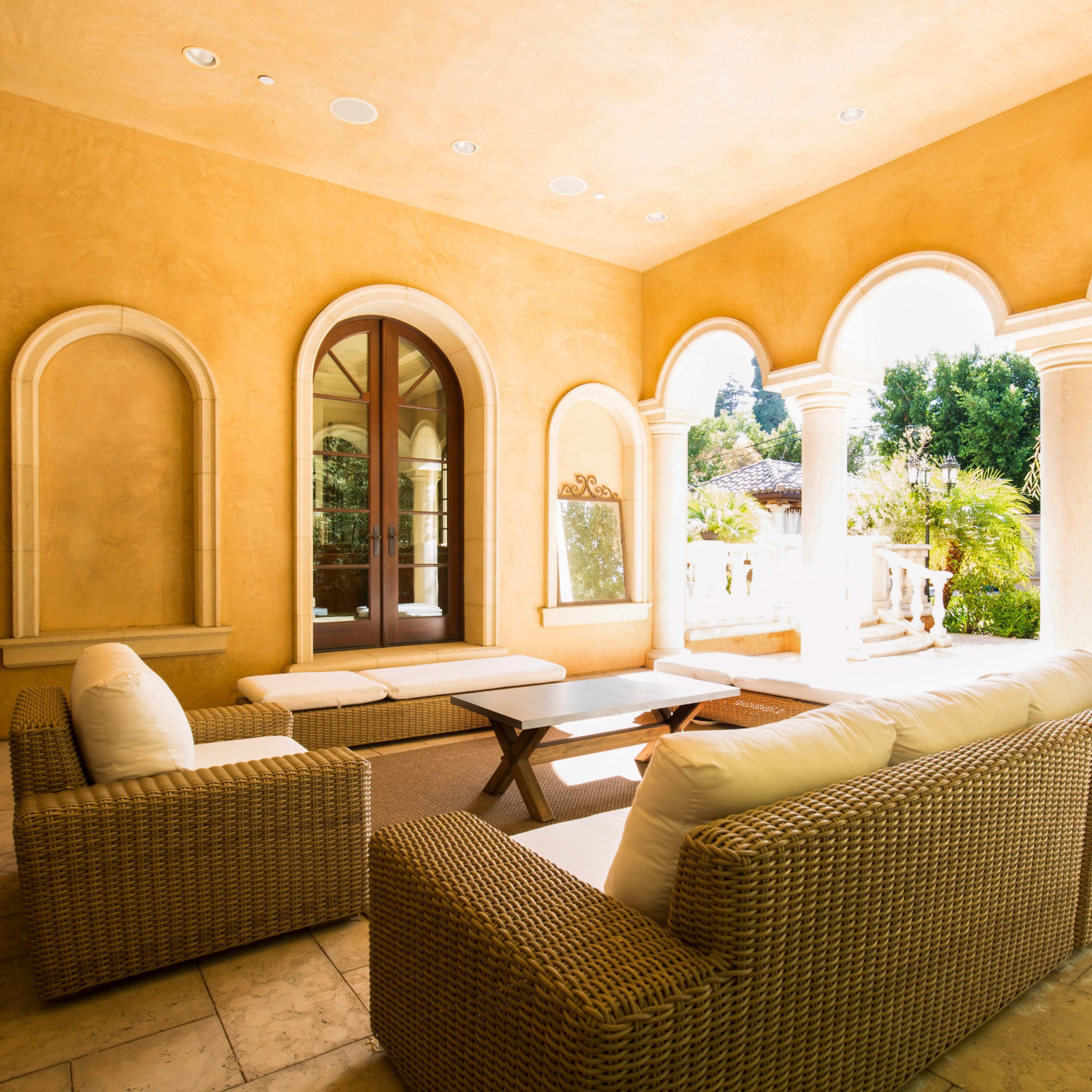 A well-lit outdoor seating area with wicker furniture and arched windows overlooking a garden.