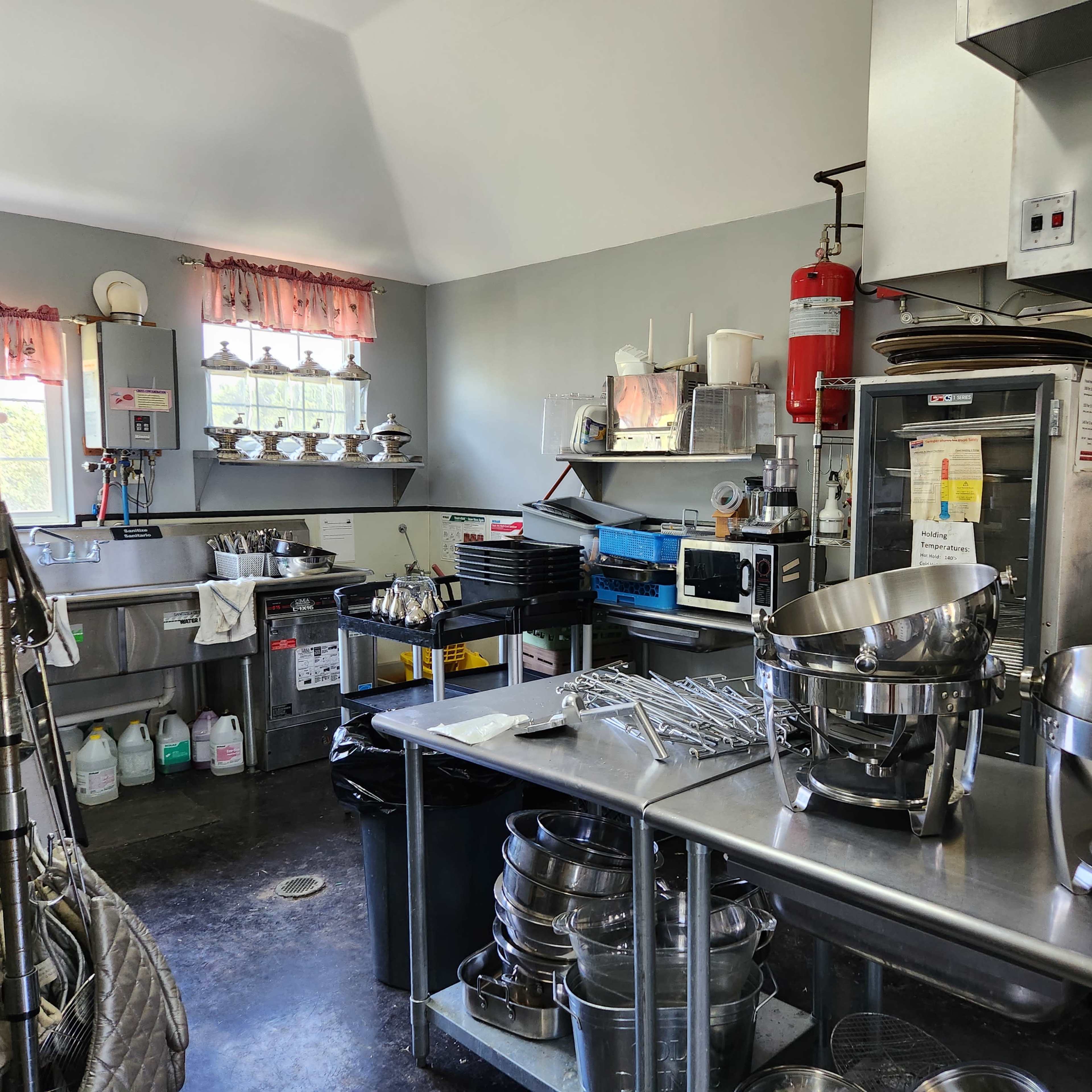 A commercial kitchen with stainless steel surfaces, various utensils, and cooking equipment organized against the walls.