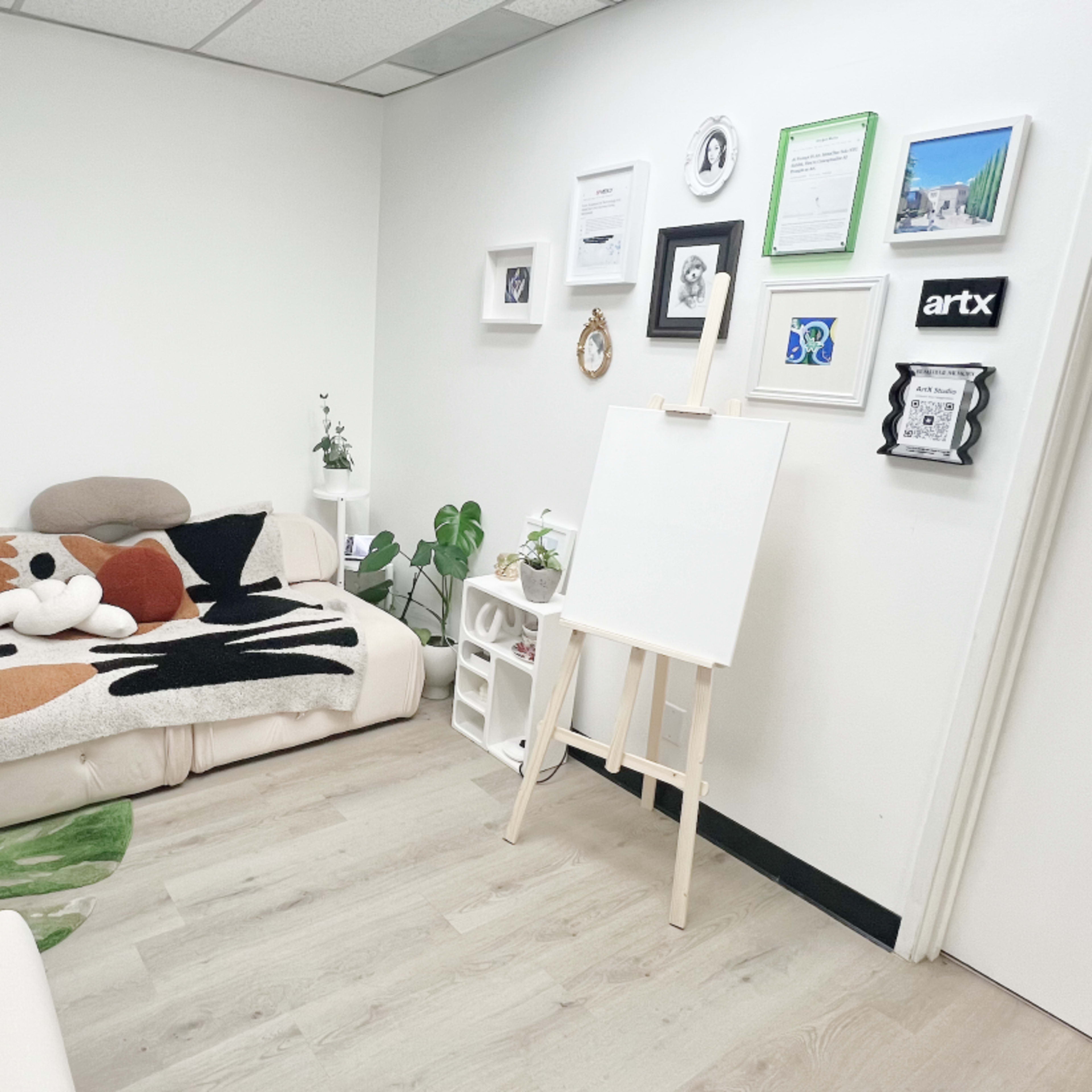 A cozy room featuring a sofa with a patterned throw, an easel, and a wall adorned with framed pictures and certificates.