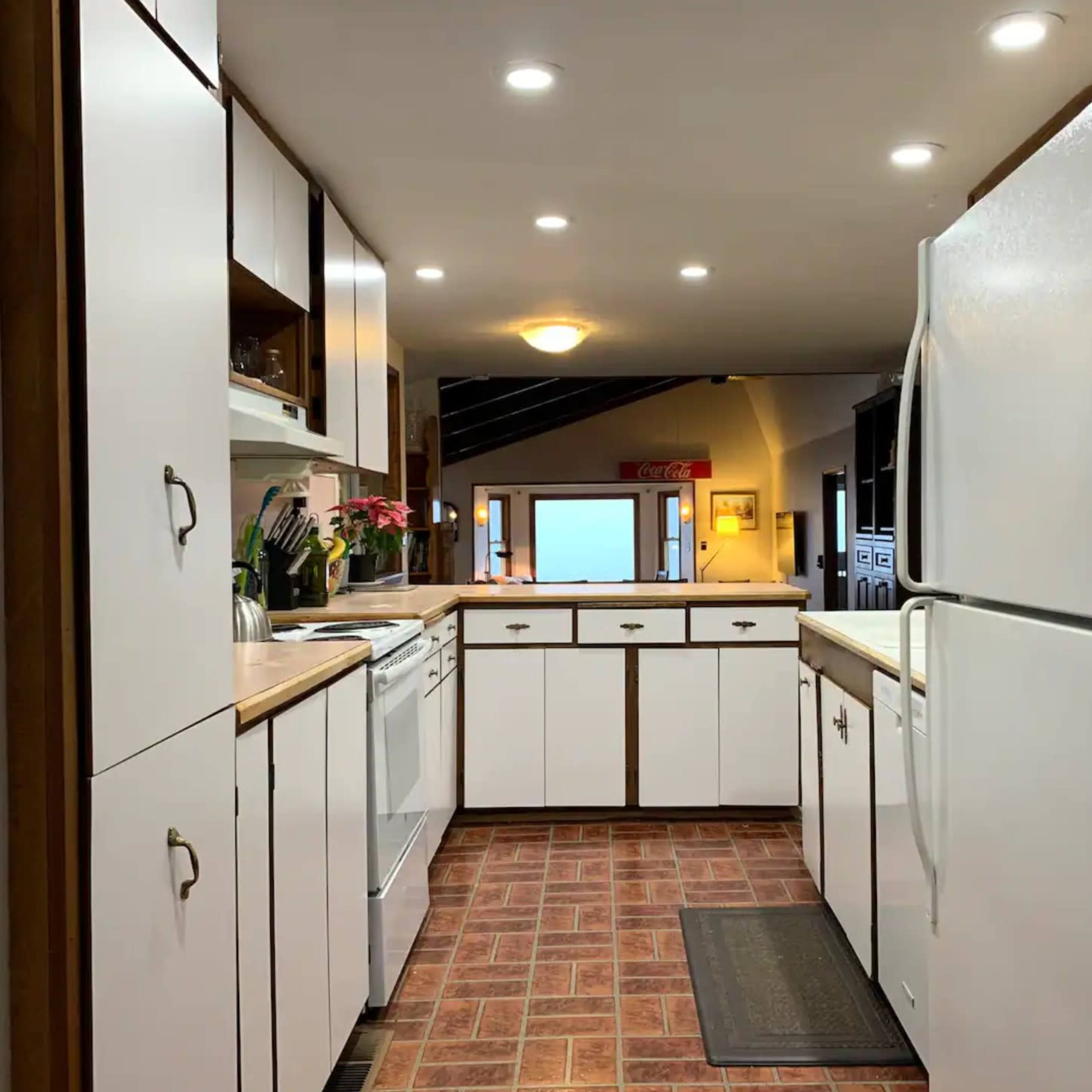 A modern kitchen with white cabinets, a refrigerator, and a view toward an external window.