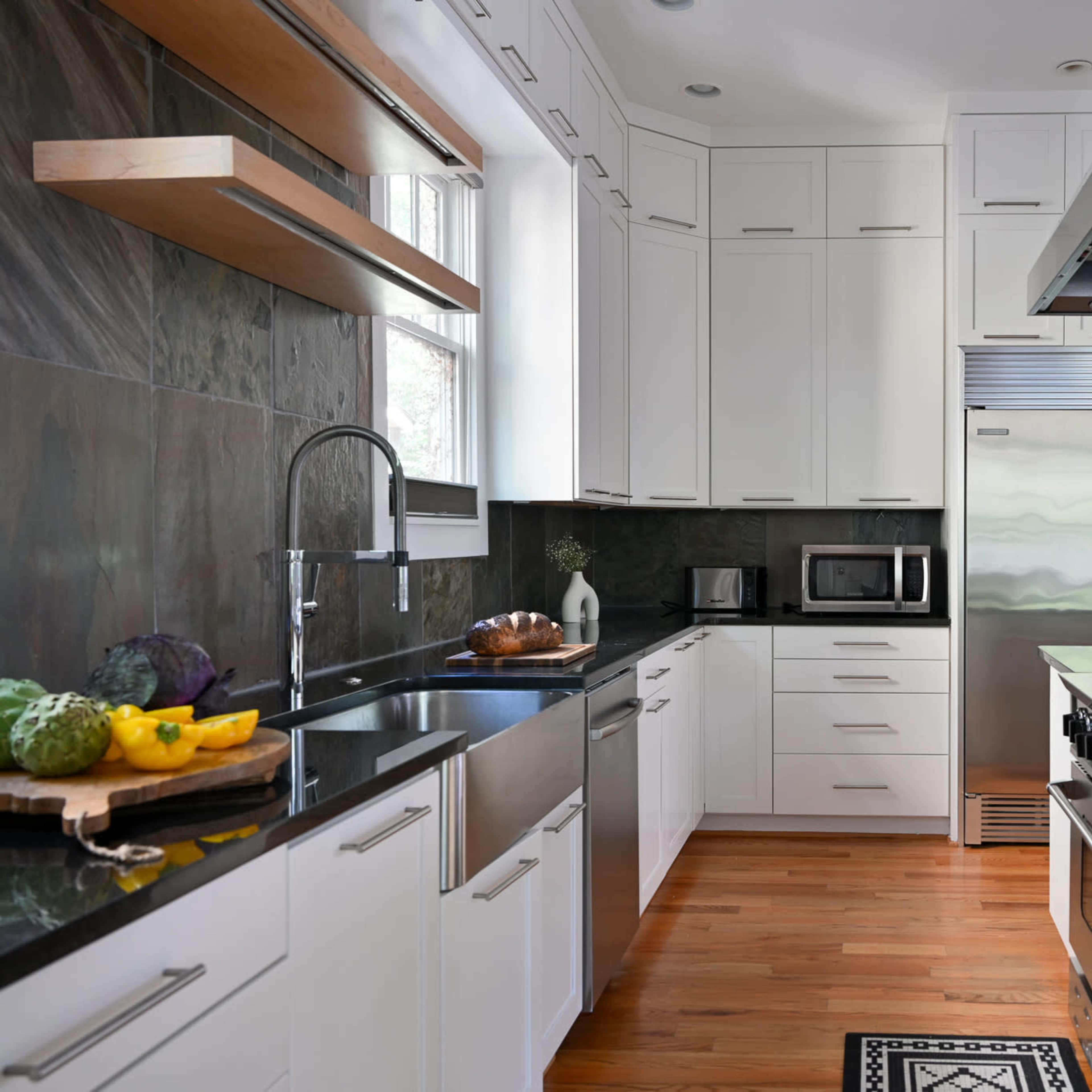 A modern kitchen features white cabinetry, stainless steel appliances, and a dark stone backsplash with wooden shelves.