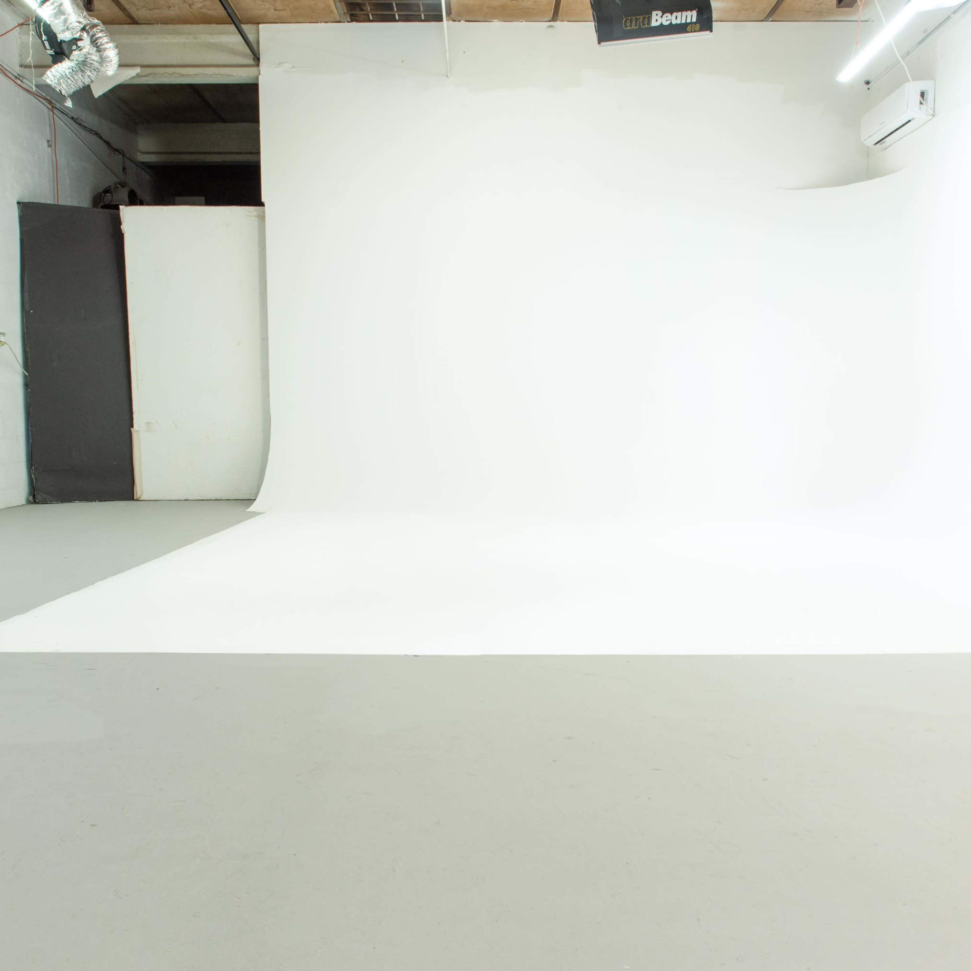 An empty studio space features a seamless white backdrop, gray flooring, and a few scattered light fixtures.