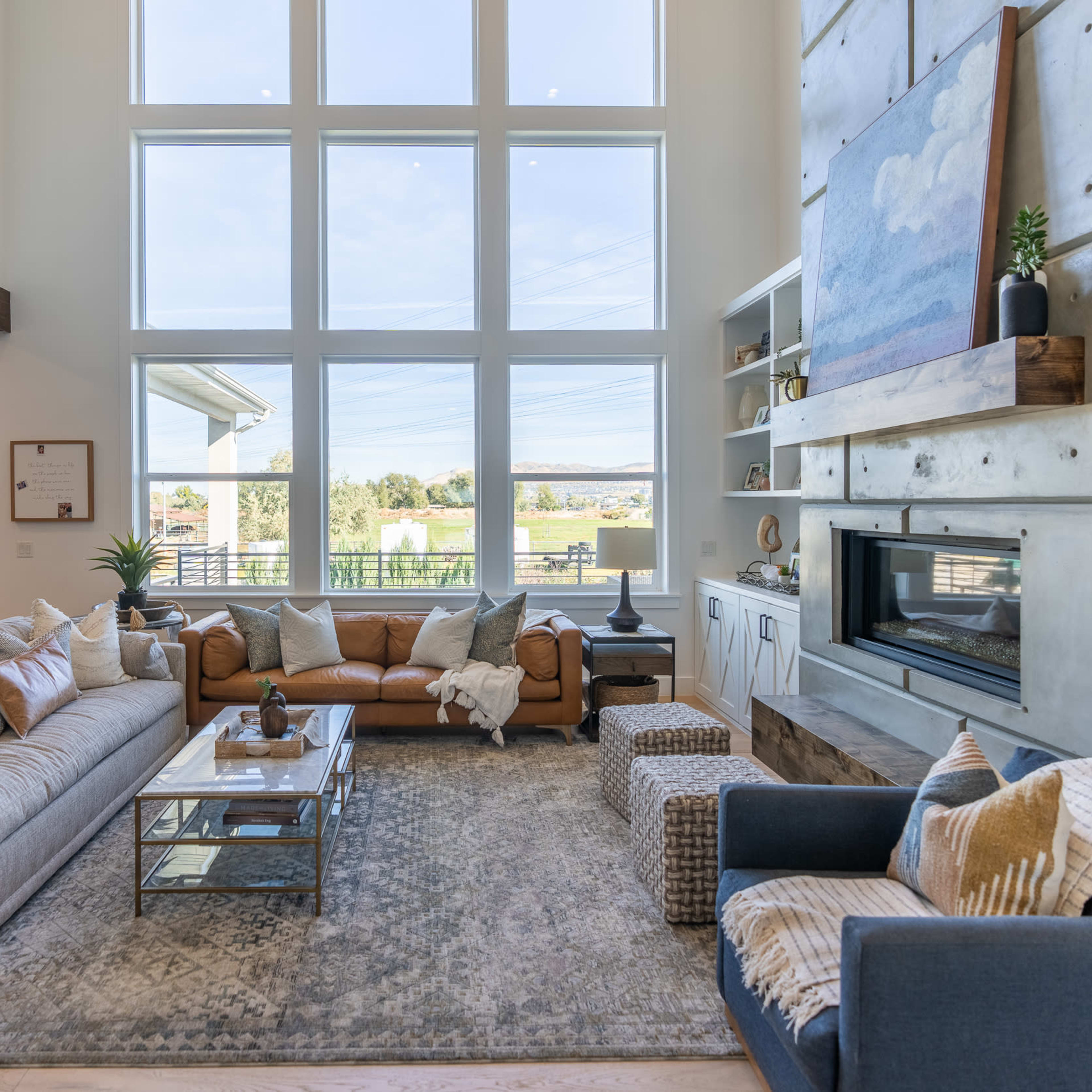 A spacious living room with large windows, a modern fireplace, and a mix of seating options including a gray sofa and a blue armchair.