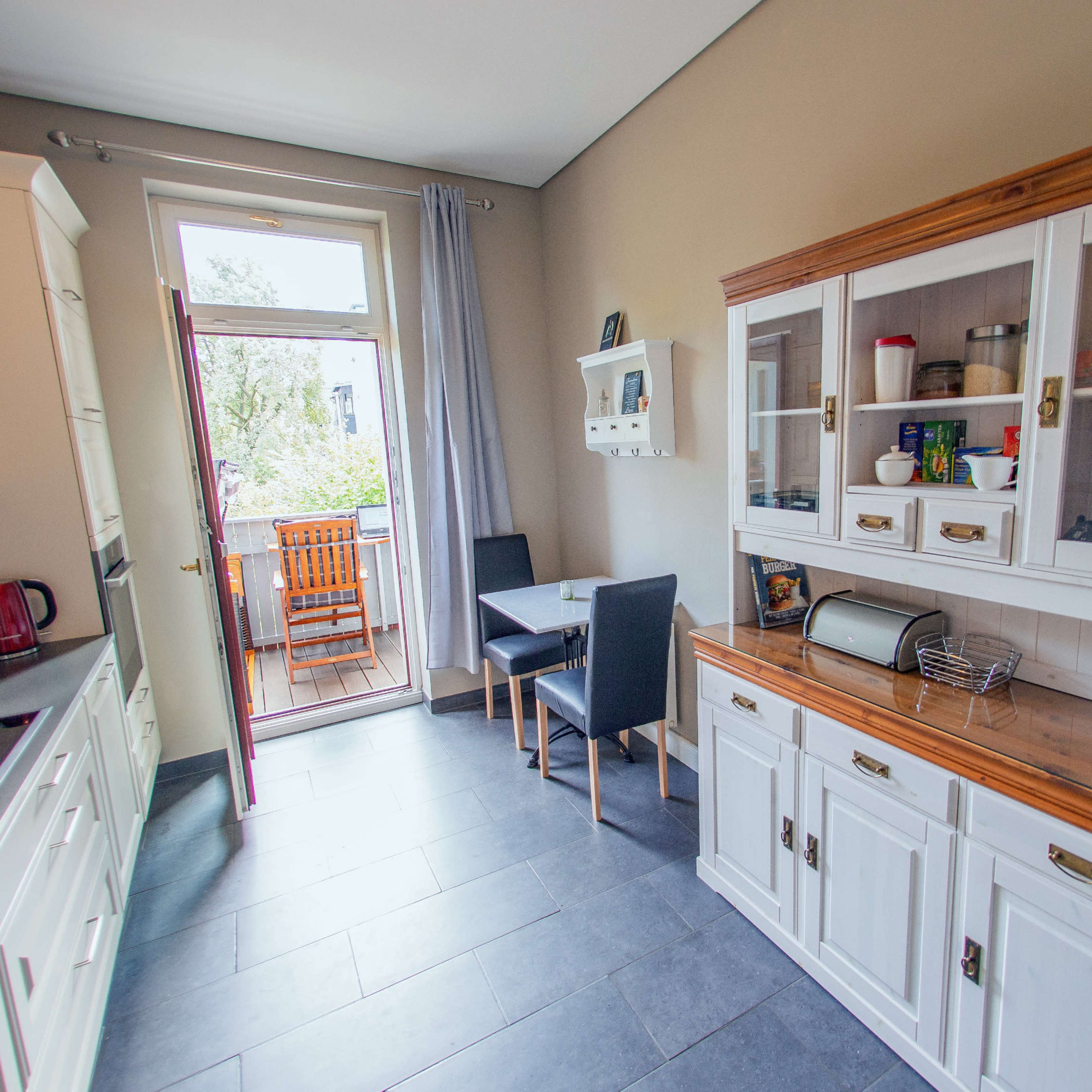 A modern kitchen with white cabinetry, a wooden dining table, and a view of an outdoor balcony.
