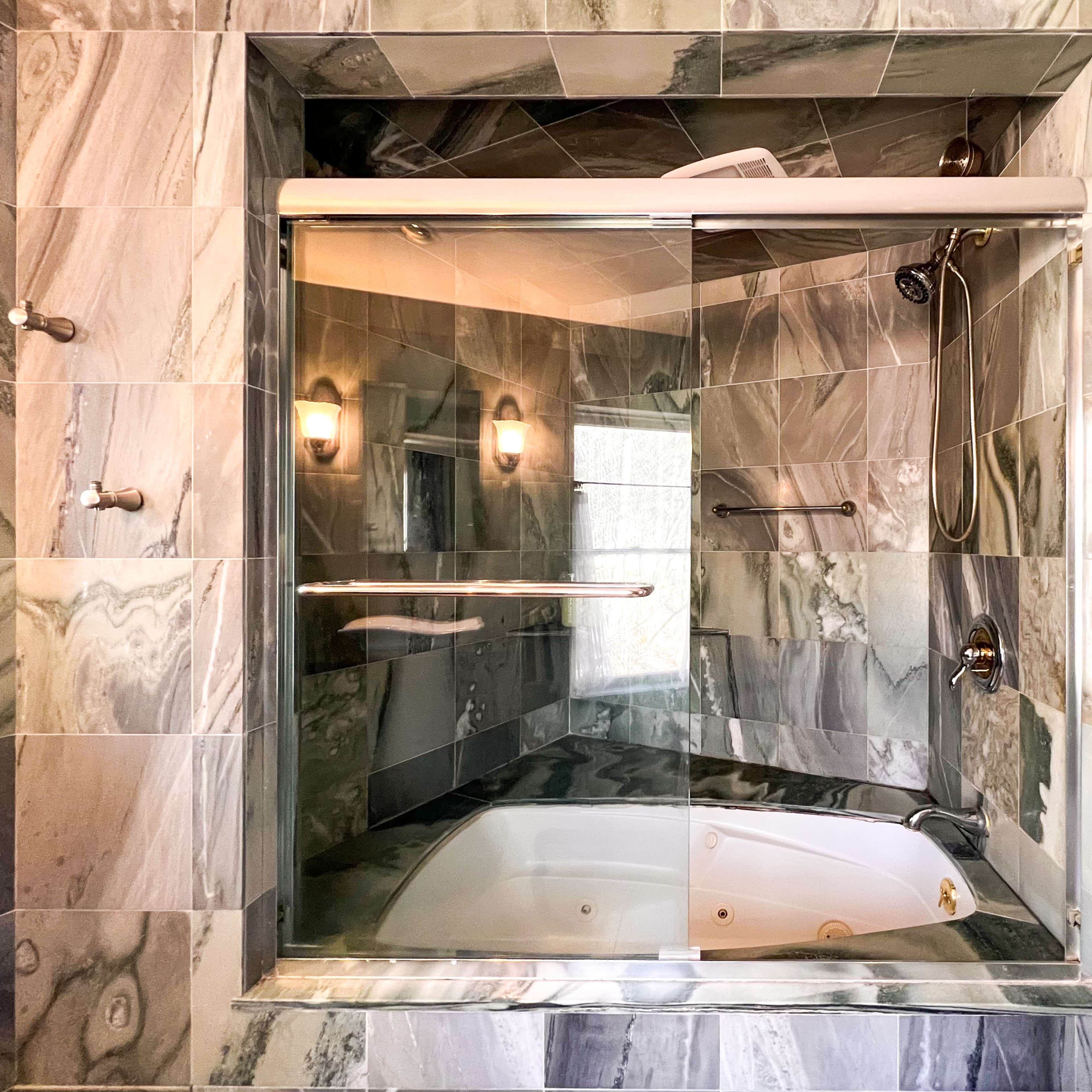 A bathroom featuring a glass-enclosed shower next to a white, oval bathtub, with walls adorned in patterned gray stone tiles.